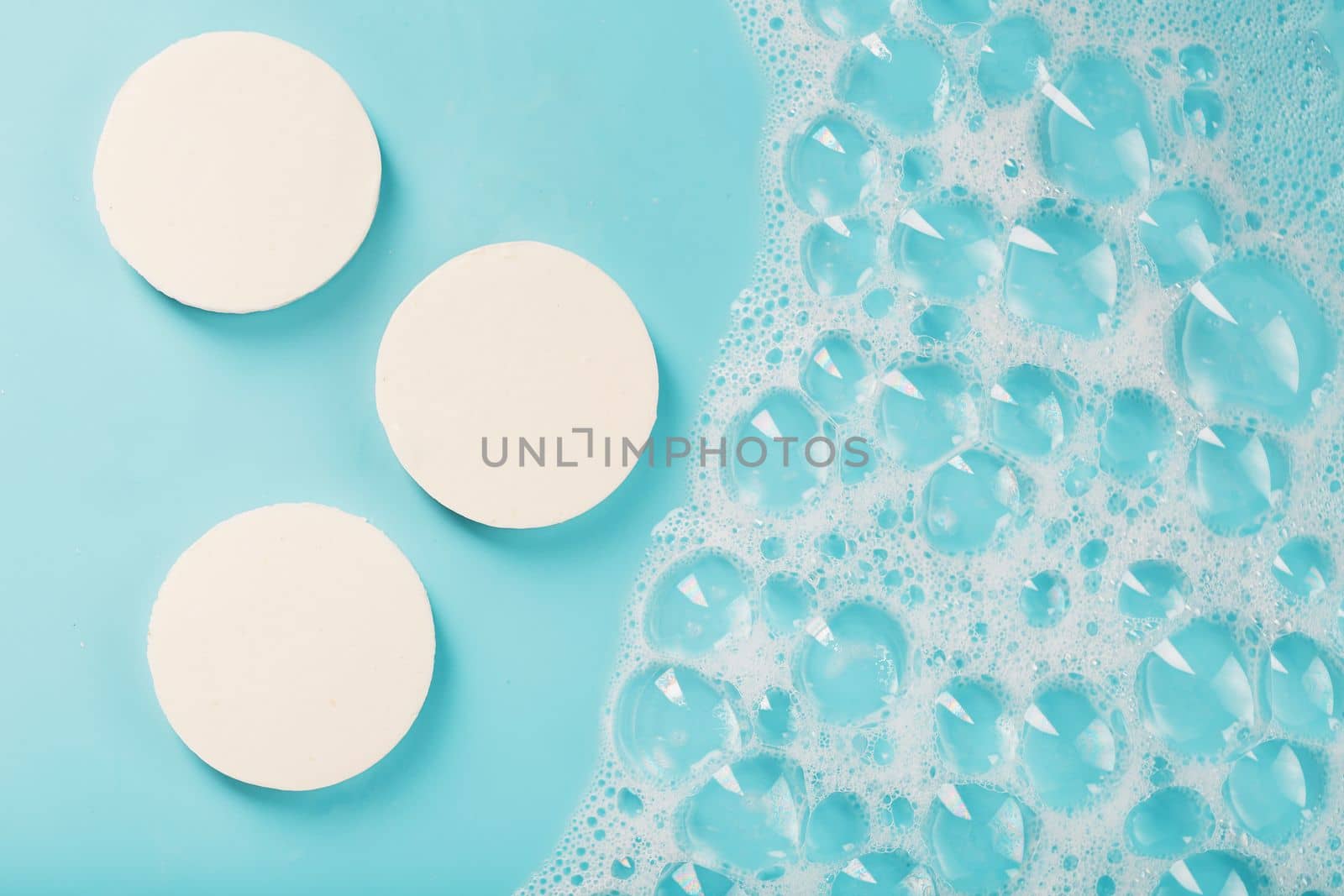 Three bars of round soap with foam on a blue background