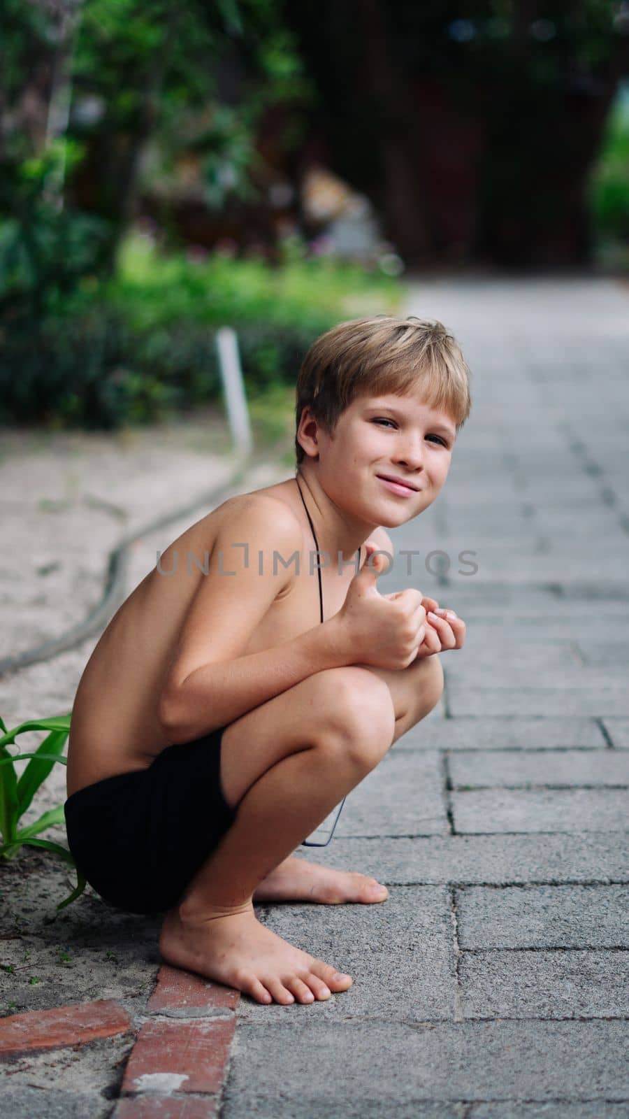 Boy blond freckles squatting sit smiling show gesture thumbs up shirtless bare chested shorts nature.