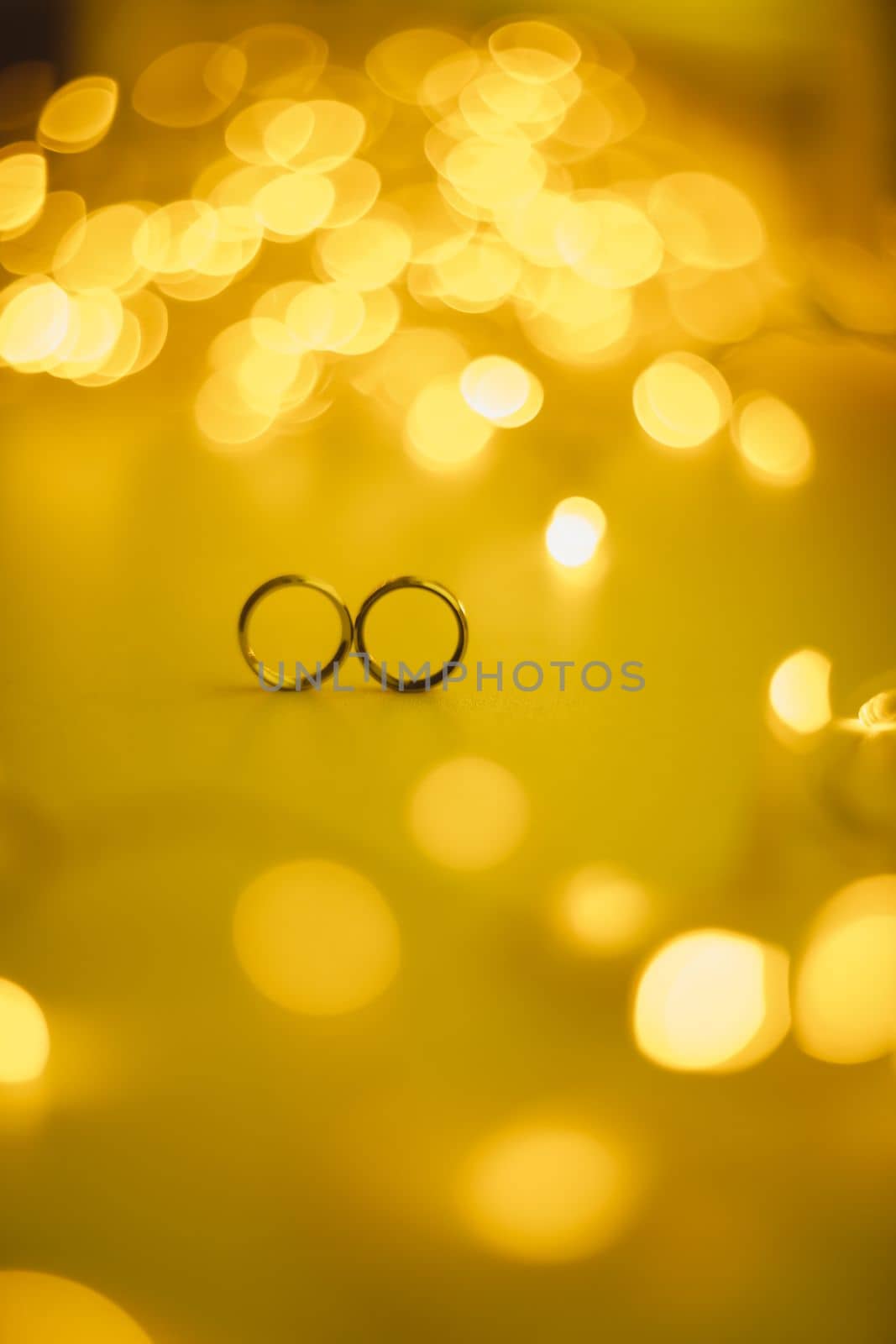 Wedding rings on blured bokeh glowing golden background. Symbol of love and romance on a textured glitter background with copy space for your greeting or congratulations.