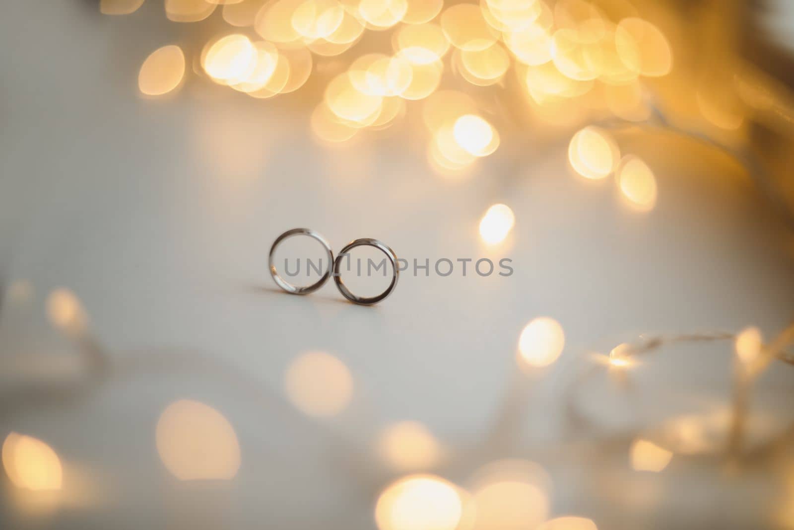 Wedding rings on blured bokeh glowing golden background. Symbol of love and romance on a textured glitter background with copy space for your greeting or congratulations.