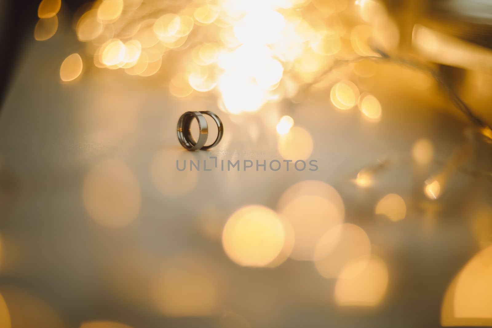 Wedding rings on blured bokeh glowing golden background. Symbol of love and romance on a textured glitter background with copy space for your greeting or congratulations by paralisart