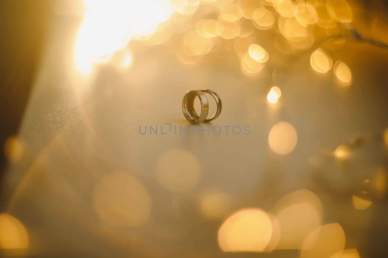 Wedding rings on blured bokeh glowing golden background. Symbol of love and romance on a textured glitter background with copy space for your greeting or congratulations by paralisart