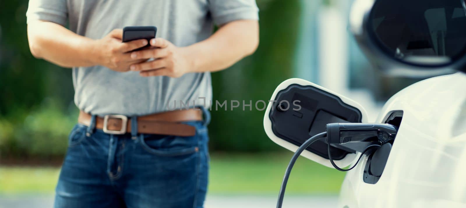 Progressive asian man install cable plug to his electric car with home charging station in the backyard. Concept use of electric vehicles in a progressive lifestyle contributes to clean environment.