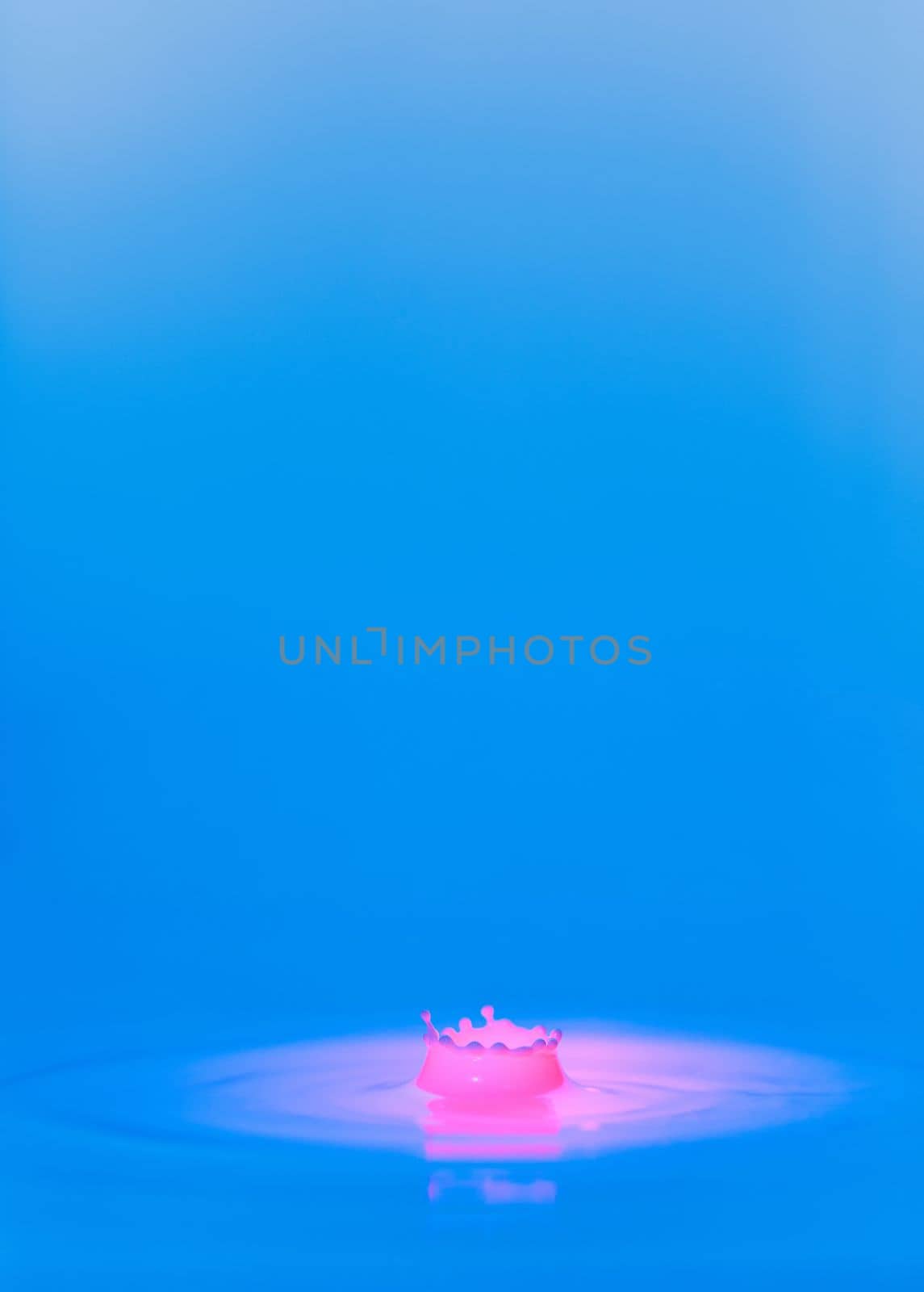 A drop falls into a thick liquid with a blue-pink background. Abstract colorful background