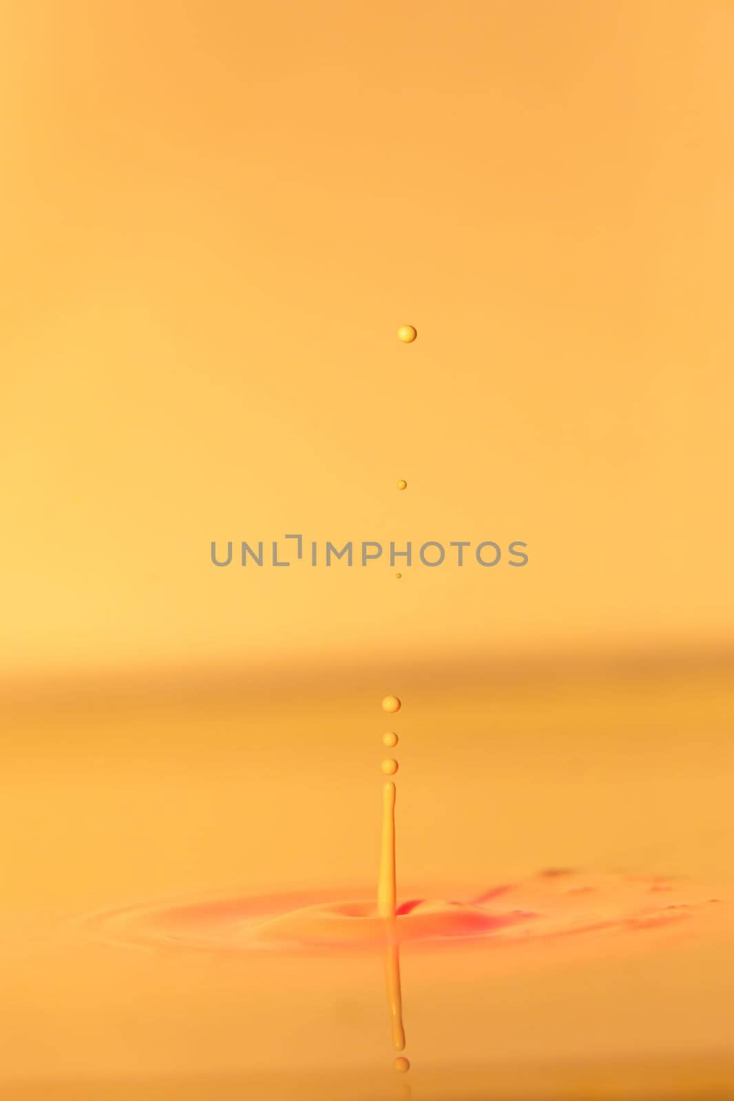 A drop falls into a thick liquid with an orange background. Abstract colorful background