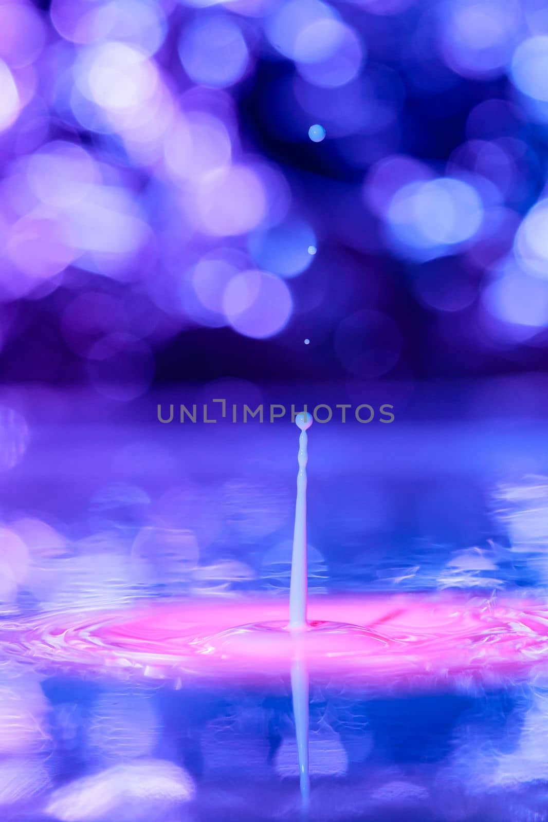 A drop falls into a thick liquid with a blue-violet background. Abstract colorful background