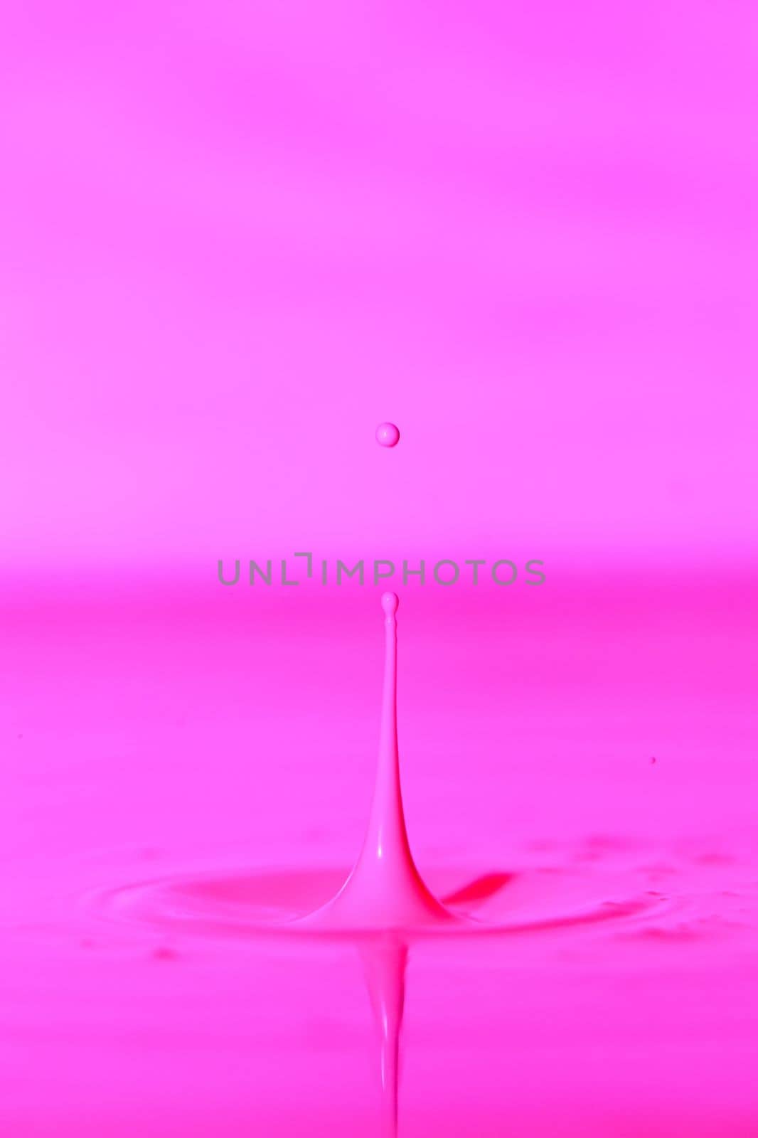 A drop falls into a thick liquid with a pink background. Abstract colorful background