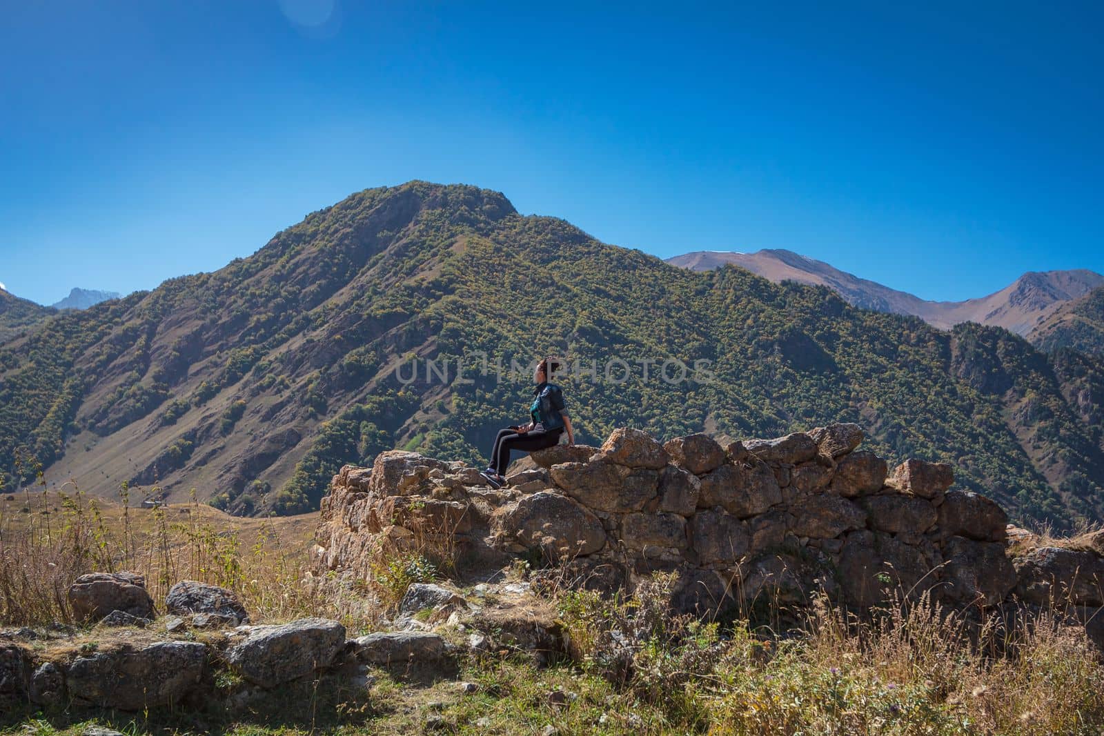 The girl sits high in the mountains on a stone and admires the views of nature