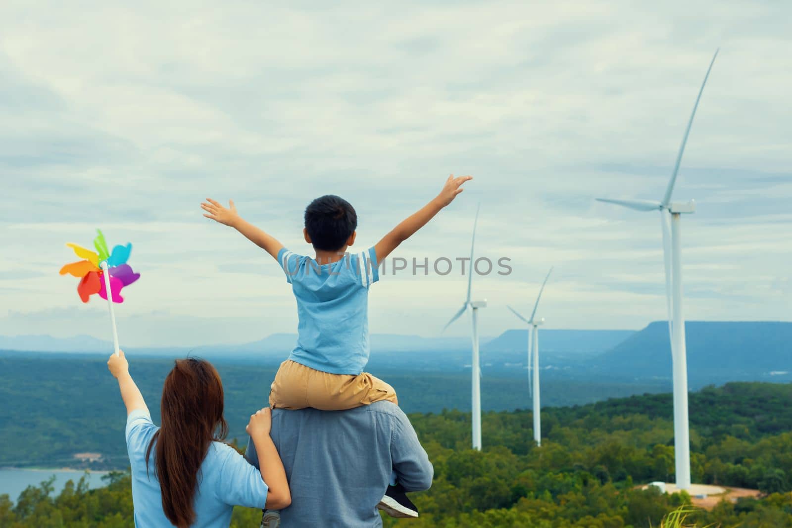 Progressive happy family enjoying their time at wind farm for green energy production concept. Wind turbine generators provide clean renewable energy for eco-friendly purposes.