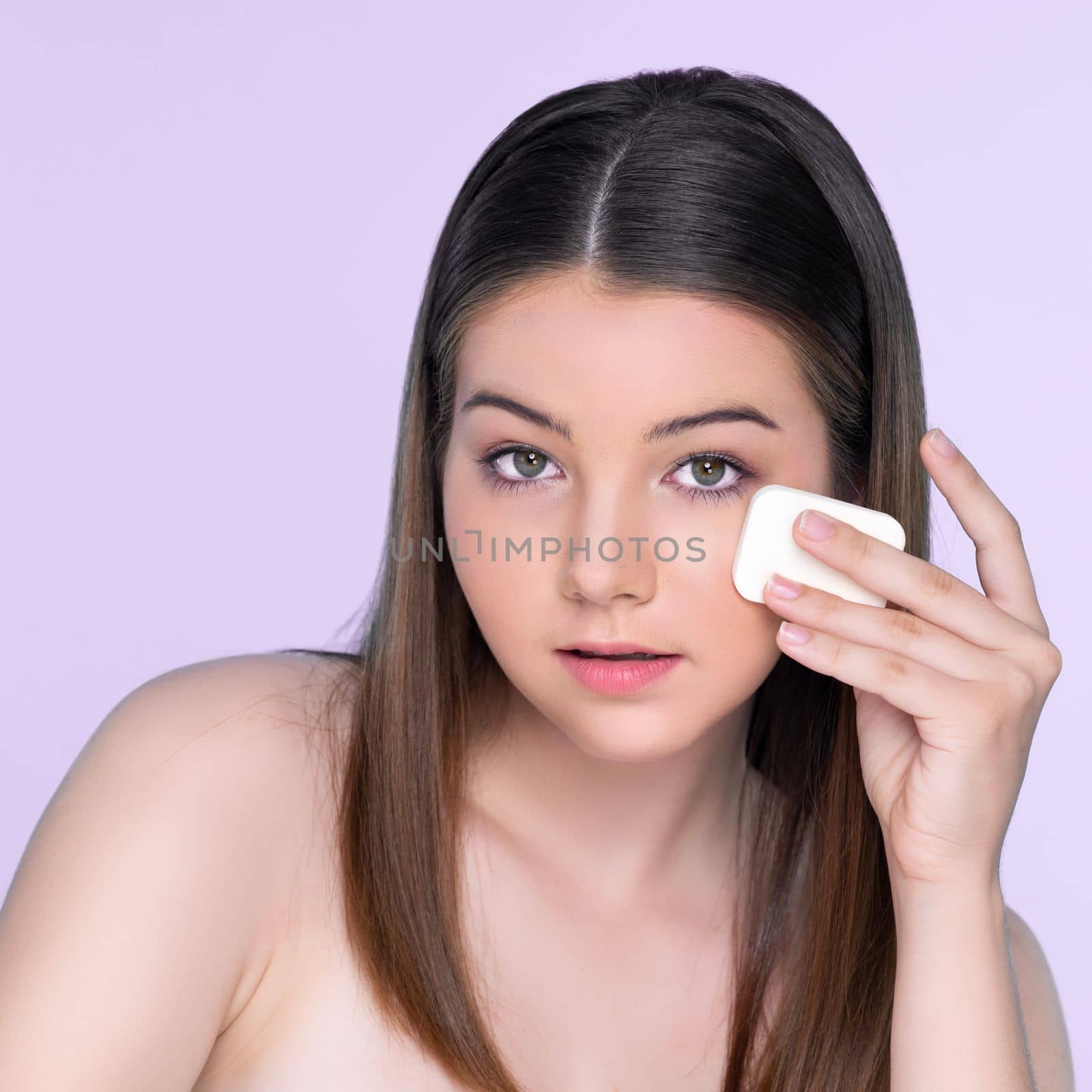 Portrait of young charming girl applying dry powder foundation on her face. by biancoblue