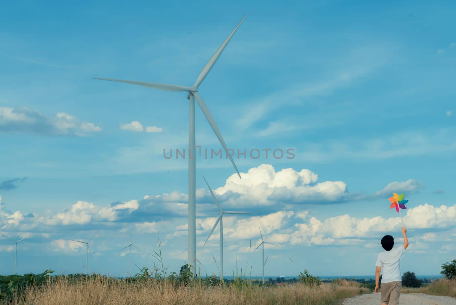 Progressive young asian boy playing with wind pinwheel toy at wind turbine farm. by biancoblue