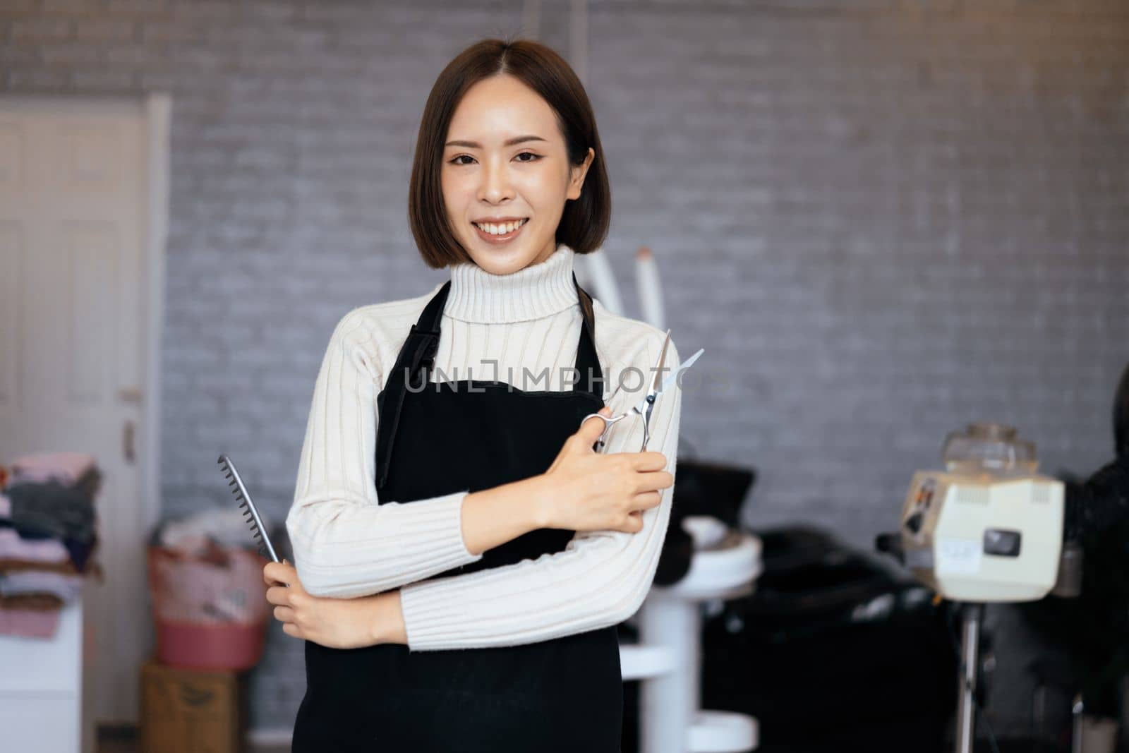 Portrait of a young asian female hairdresser holding qualified haircut tools in her salon for a woman's haircut. Photo job concept for small business owner and haircare.