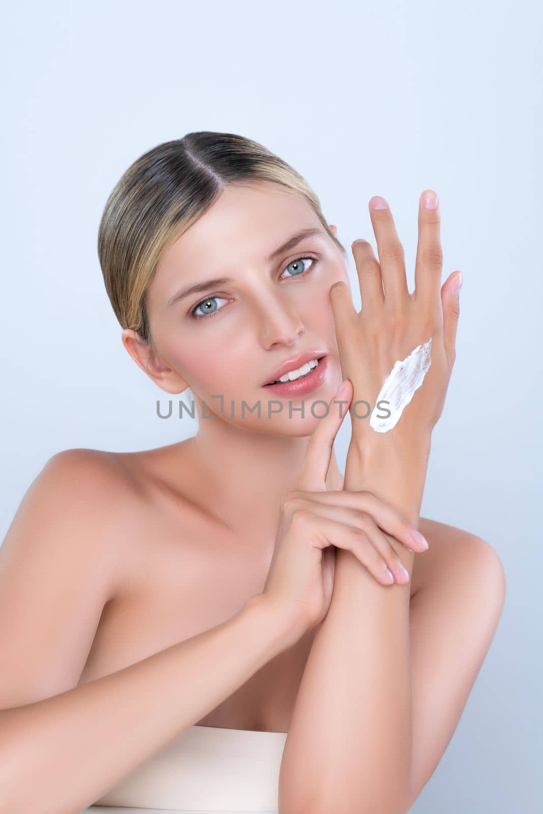 Alluring beautiful woman applying moisturizer cream on her hand for perfect skincare treatment in isolated background. Caucasian women portrait with skin rejuvenation and cosmetology concept.