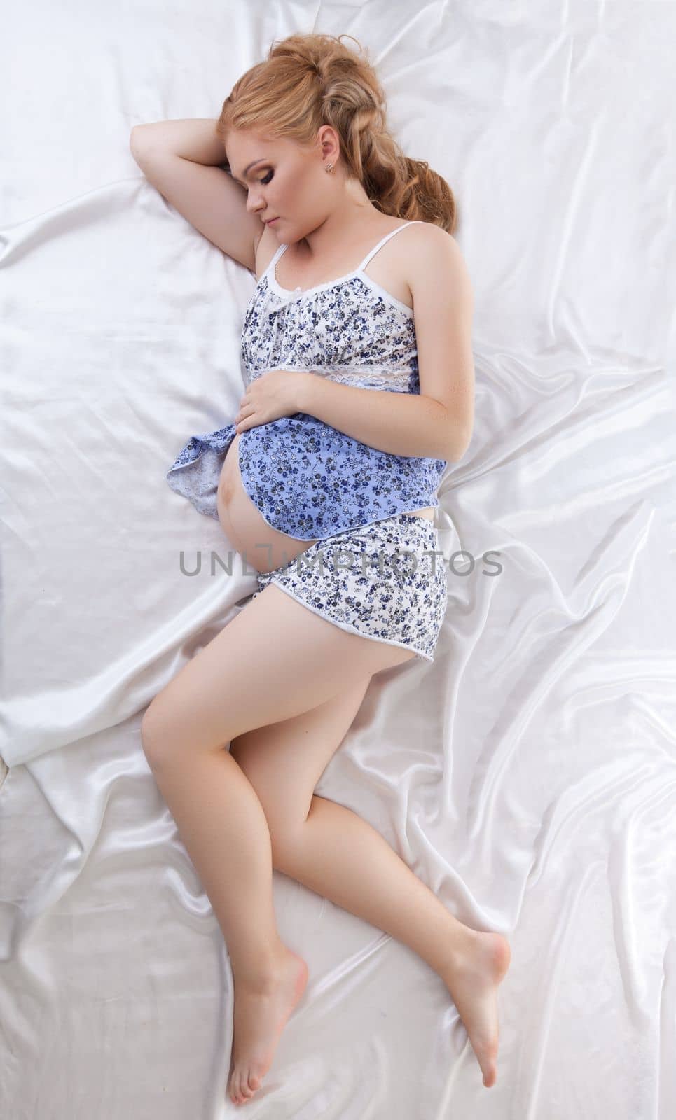 Beautiful pregnant woman sleeping in silk bed top view