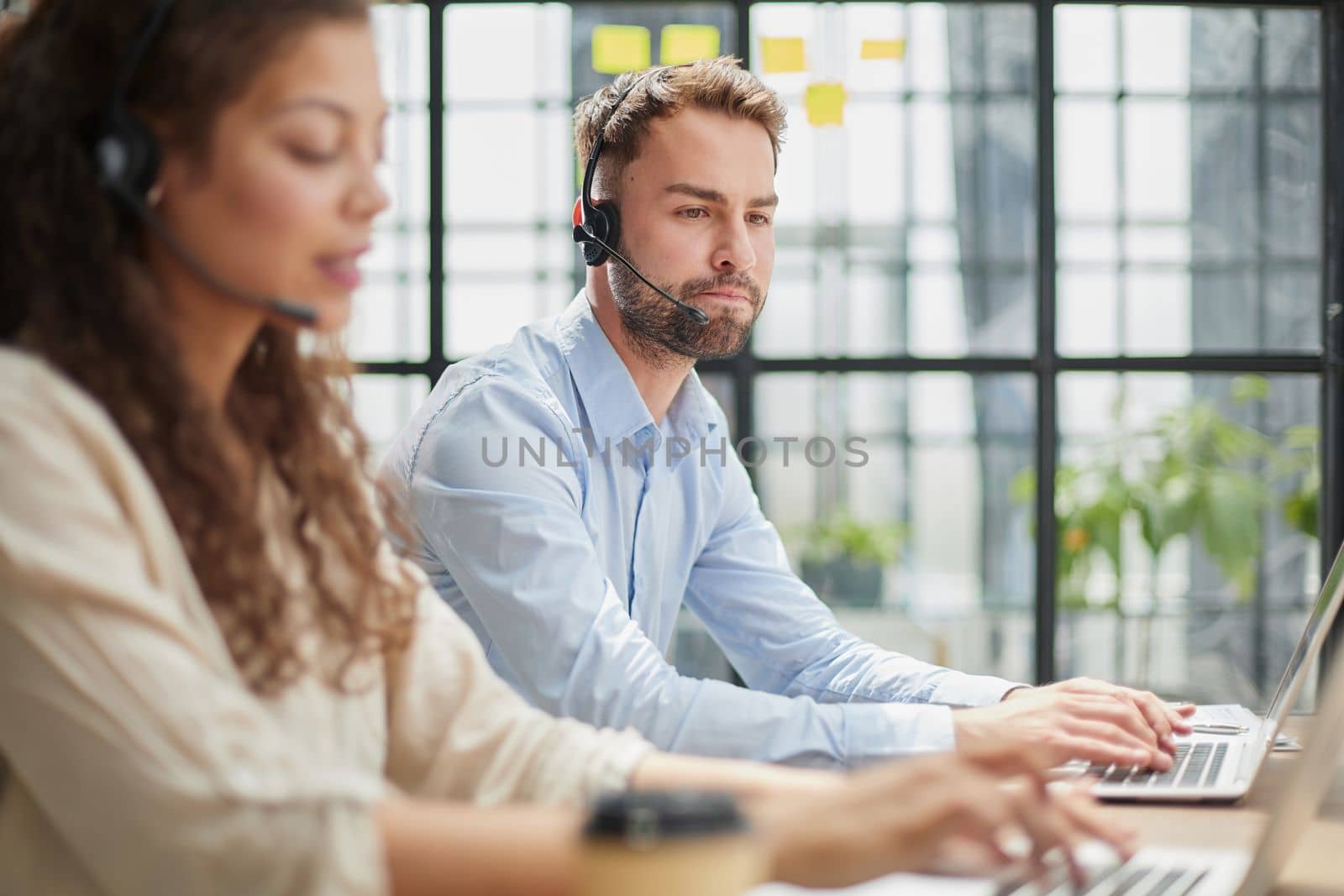 male call-center operator with headphones sitting at modern office, consulting online information in a laptop, looking up information in a file in order to be of assistance to the client.