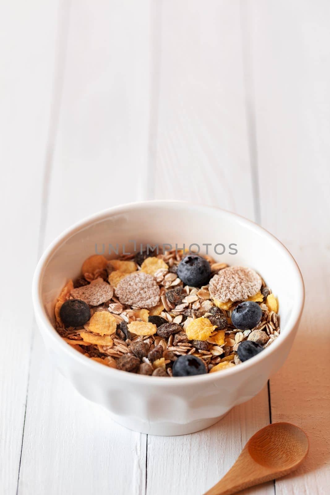 breakfast bowl of oat, corn and spelled flakes and fresh berries on the white wooden table, copy space