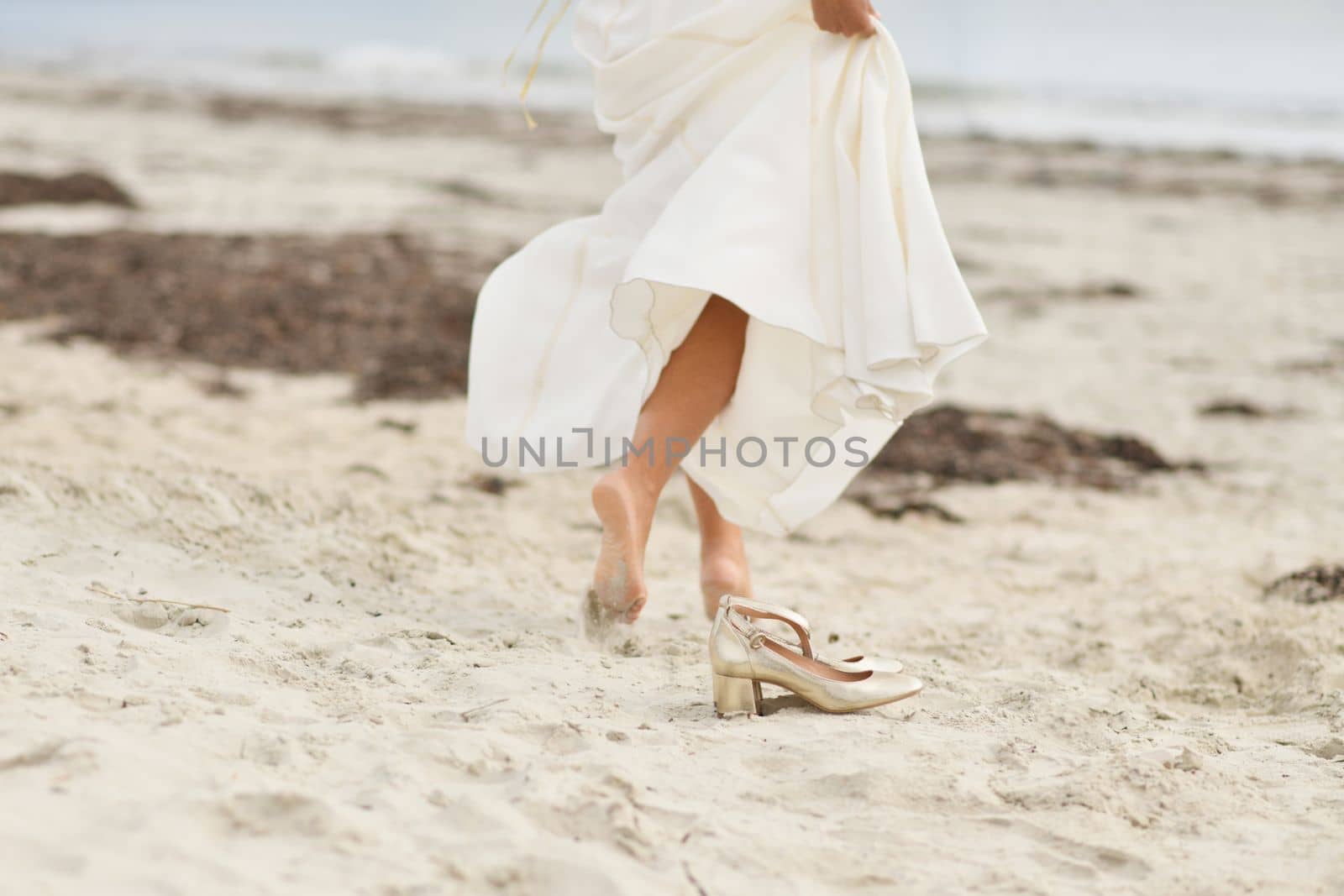 Bride in white dress and golden shoes on the sandy beach