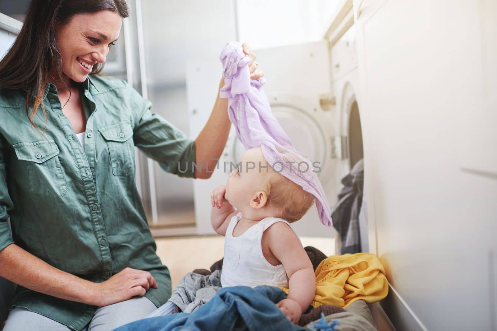 Youre not laundry. a baby girl sitting in a laundry basket while her mother does the washing. by YuriArcurs