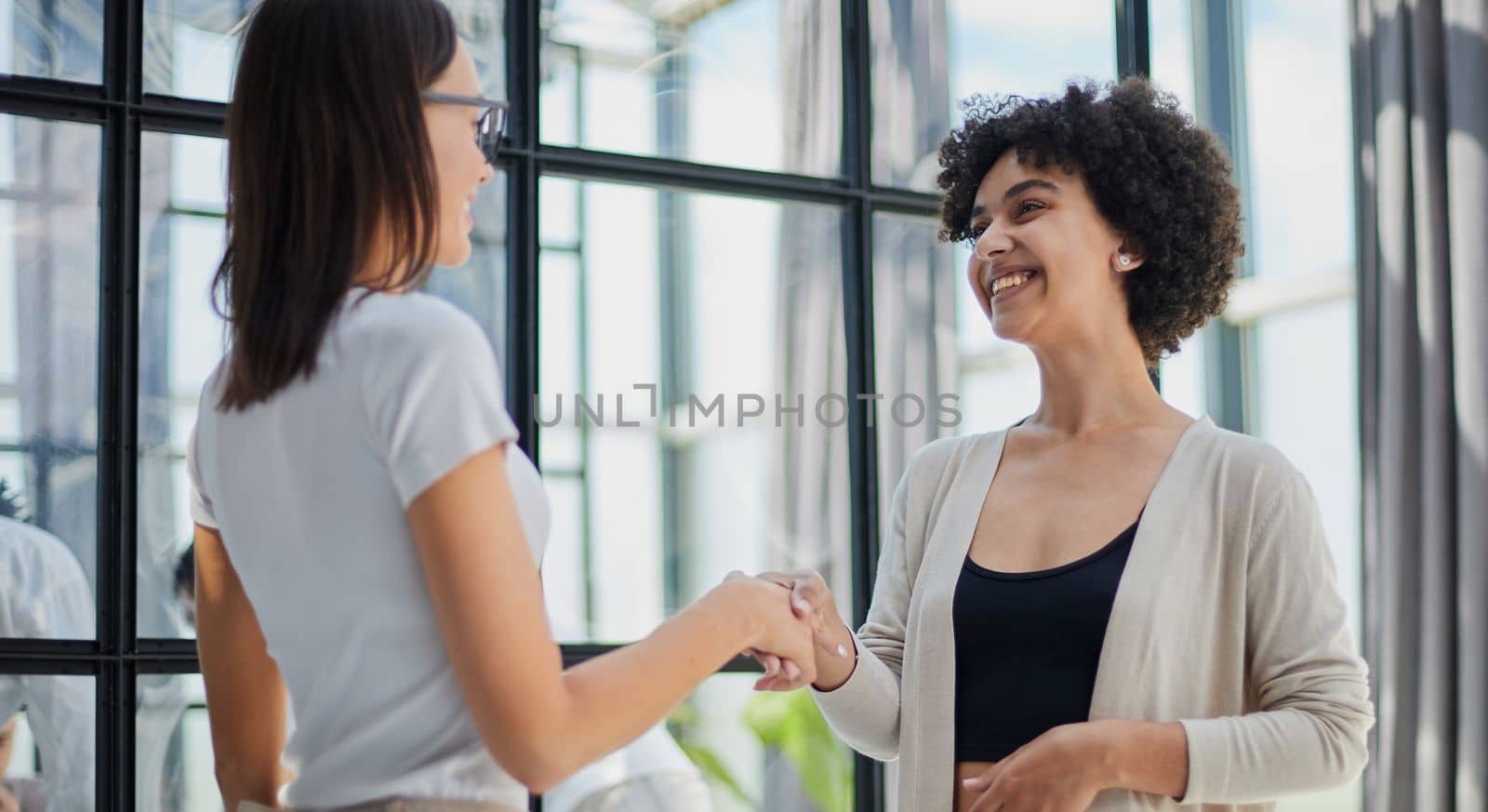 Two middle age beautiful businesswomen smiling happy and confident working together. Shaking hands with smile on face for agreement at the office