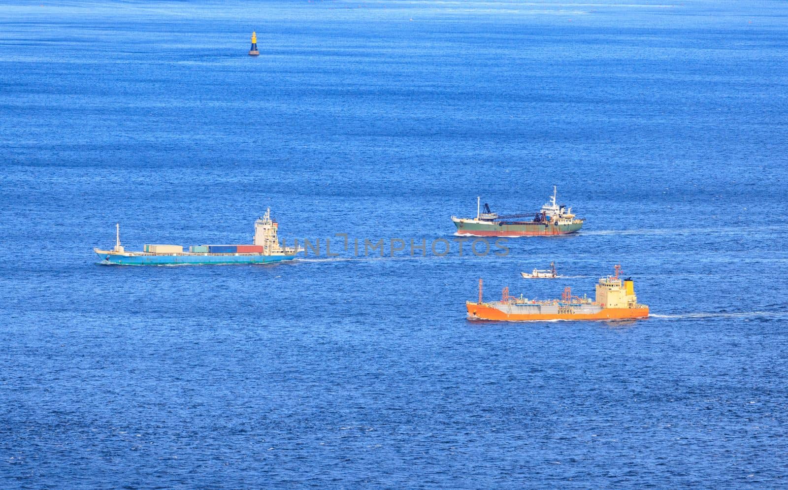 Small Fleet of Cargo Ships Sail through Shipping Lane in Calm Blue Sea by Osaze