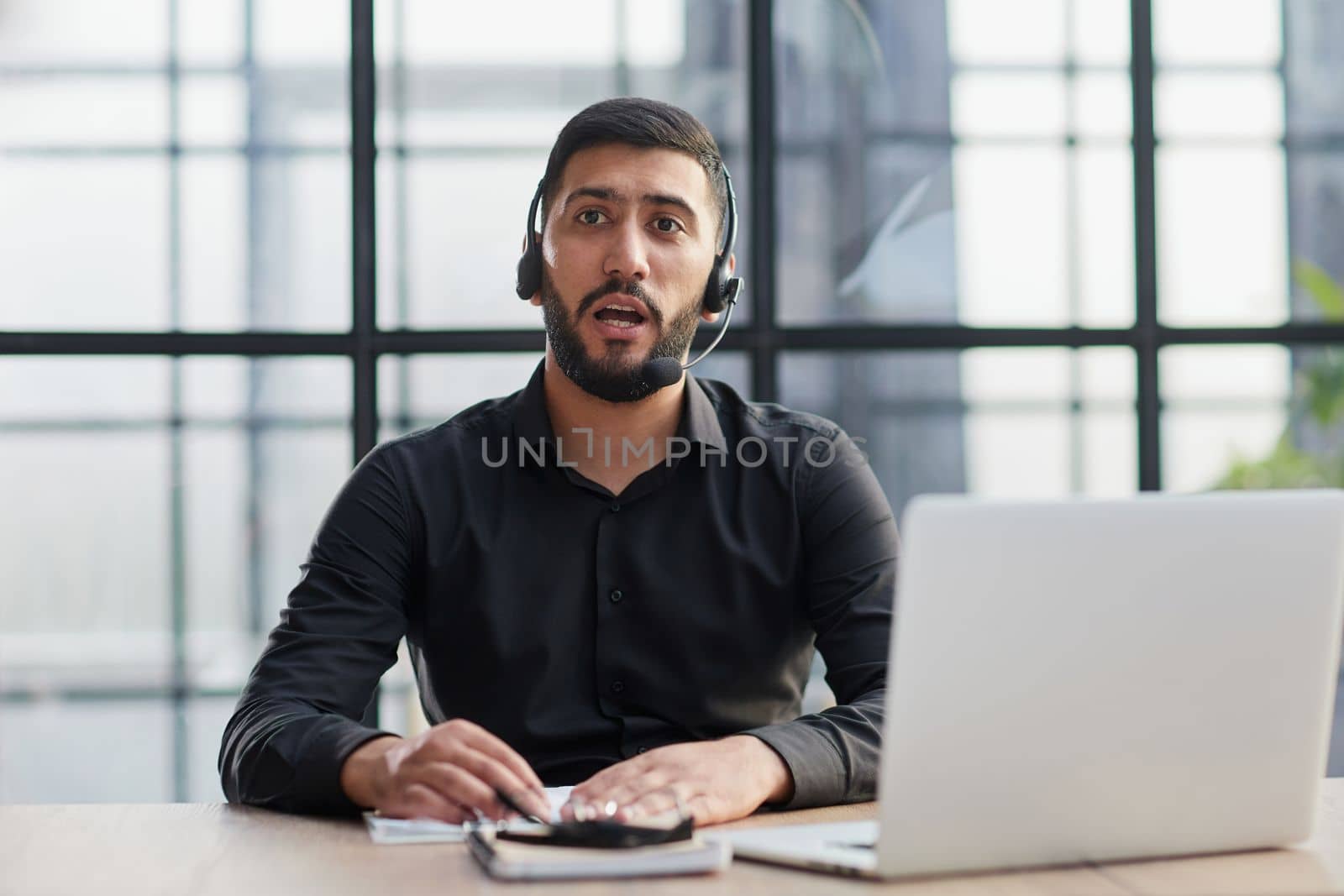 Young handsome male customer support phone operator with headset working in his office.