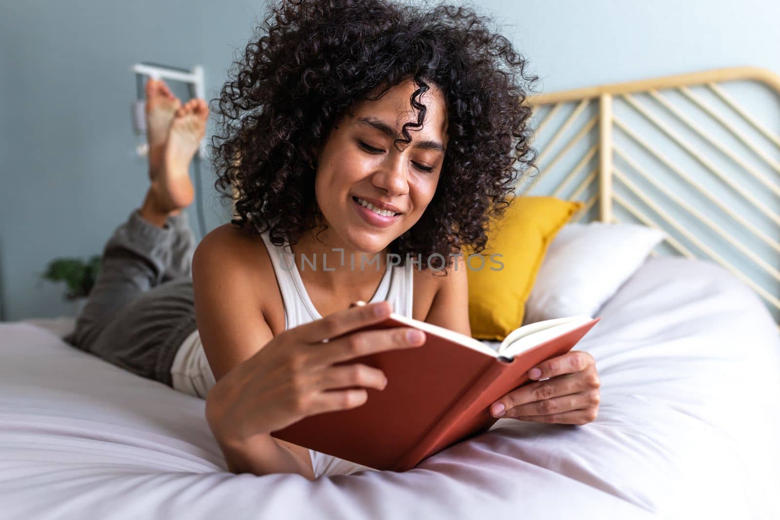 Happy young multiracial woman lying on the bed reading a book relaxing at home. Lifestyle concept.