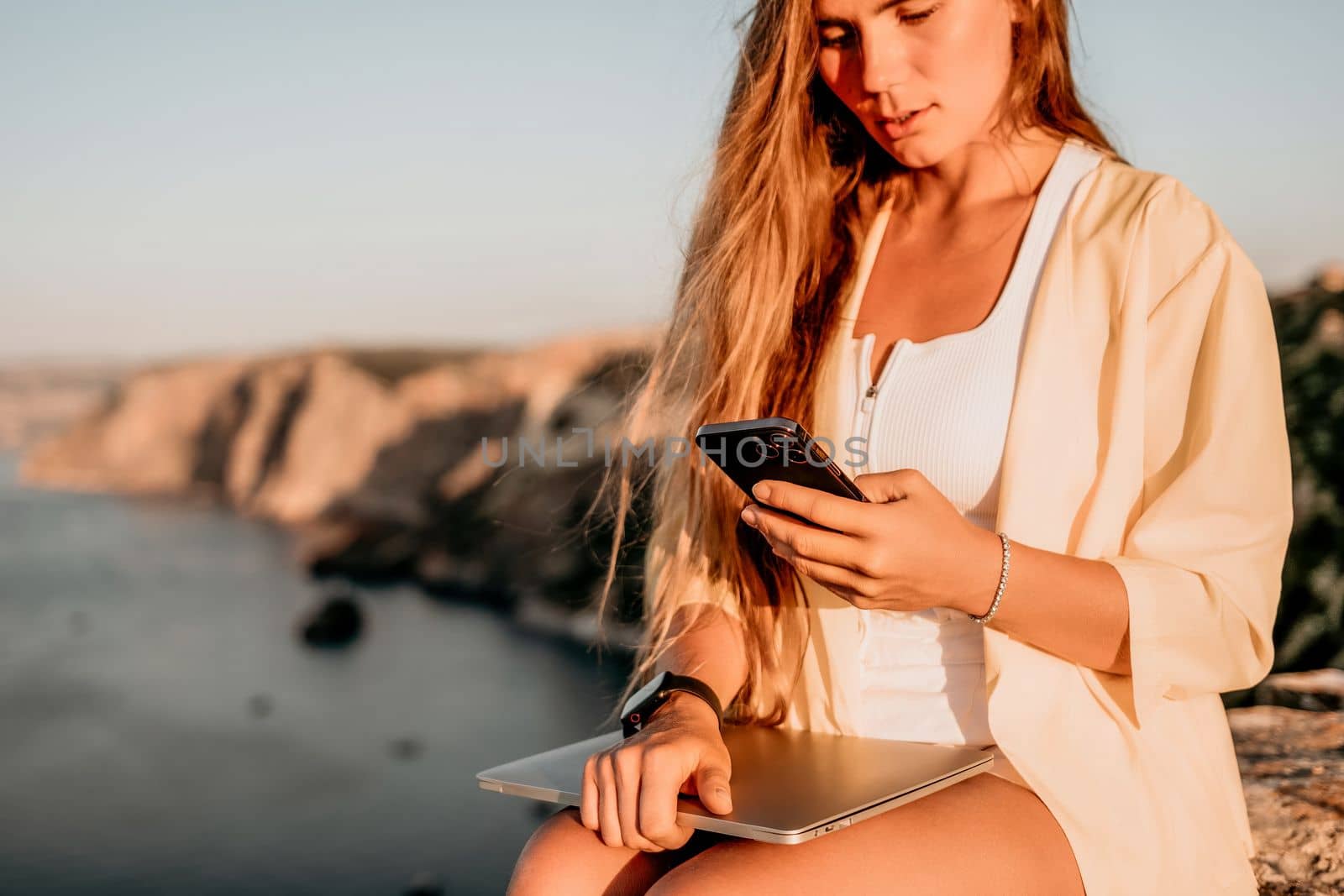 Successful business woman in yellow hat working on laptop by the sea. Pretty lady typing on computer at summer day outdoors. Freelance, travel and holidays concept.