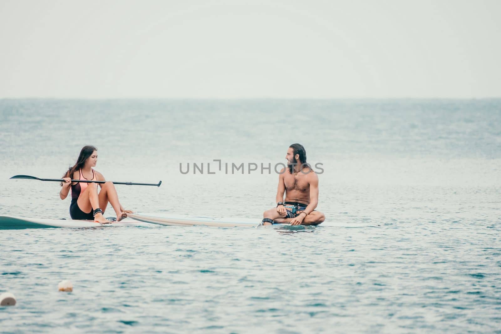 Sea woman and man on sup. Silhouette of happy young woman and man, surfing on SUP board, confident paddling through water surface. Idyllic sunset. Active lifestyle at sea or river