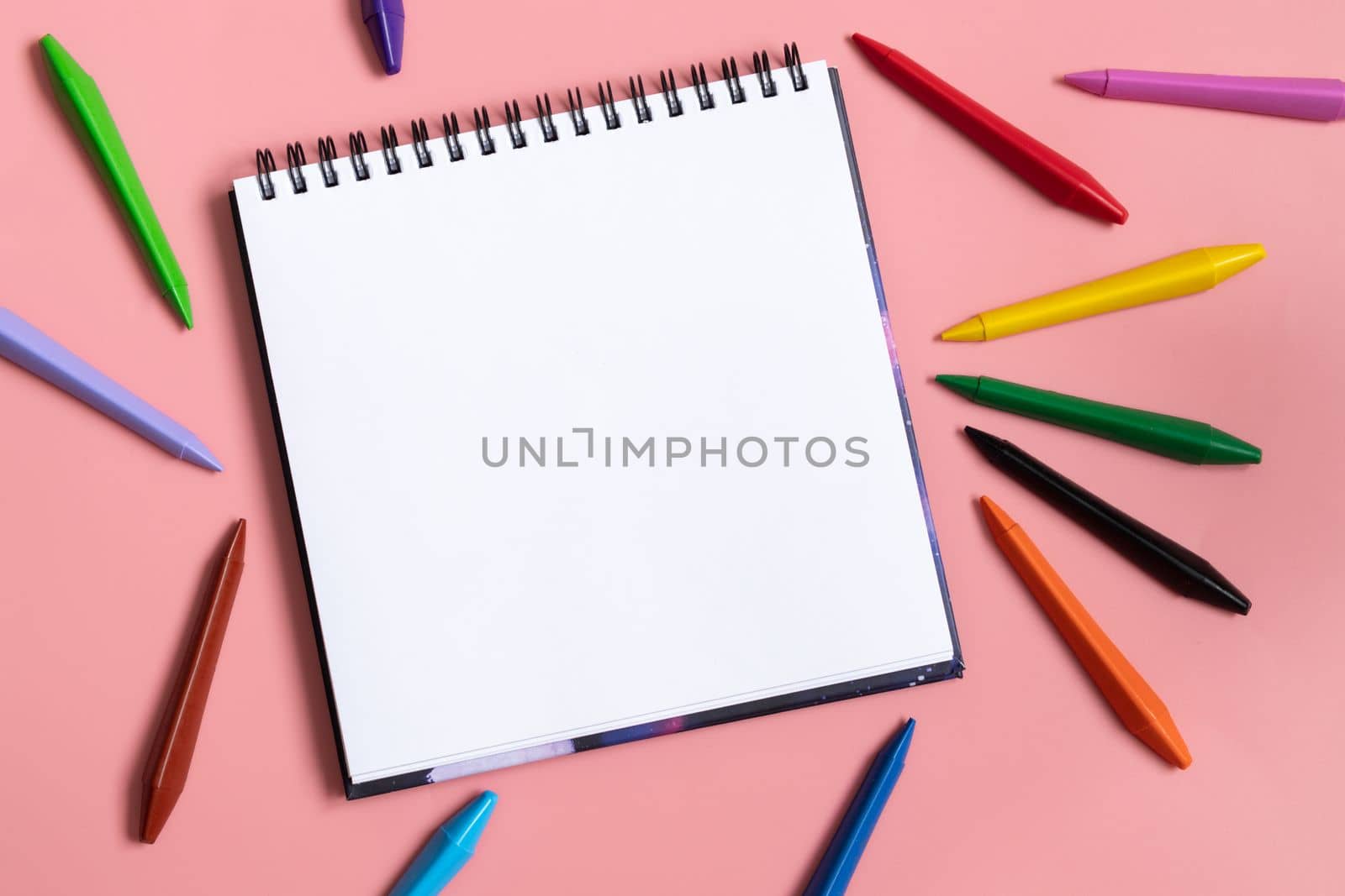 Mock up of empty scketchbook white paper on pastel pink background. Colorful wax crayons. Top view of open notebook with clean sheet. Template art. Copy space