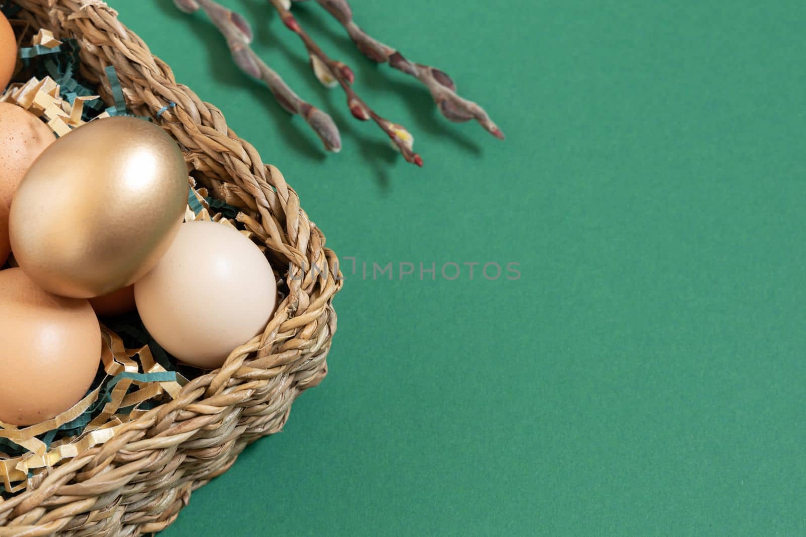 Easter eggs with funny face natural and gold in basket with paper filler . Branch of willow catkins. Light pastel orange background with copy space.