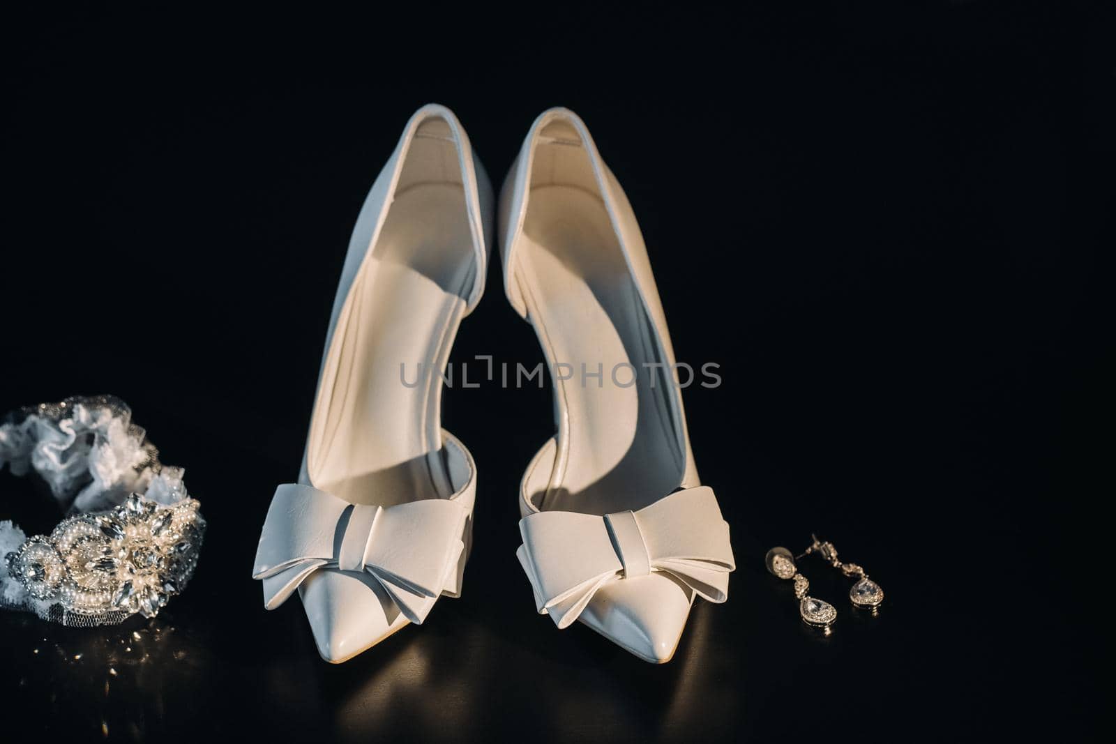 white wedding shoes and garter belt with earrings on a black background.
