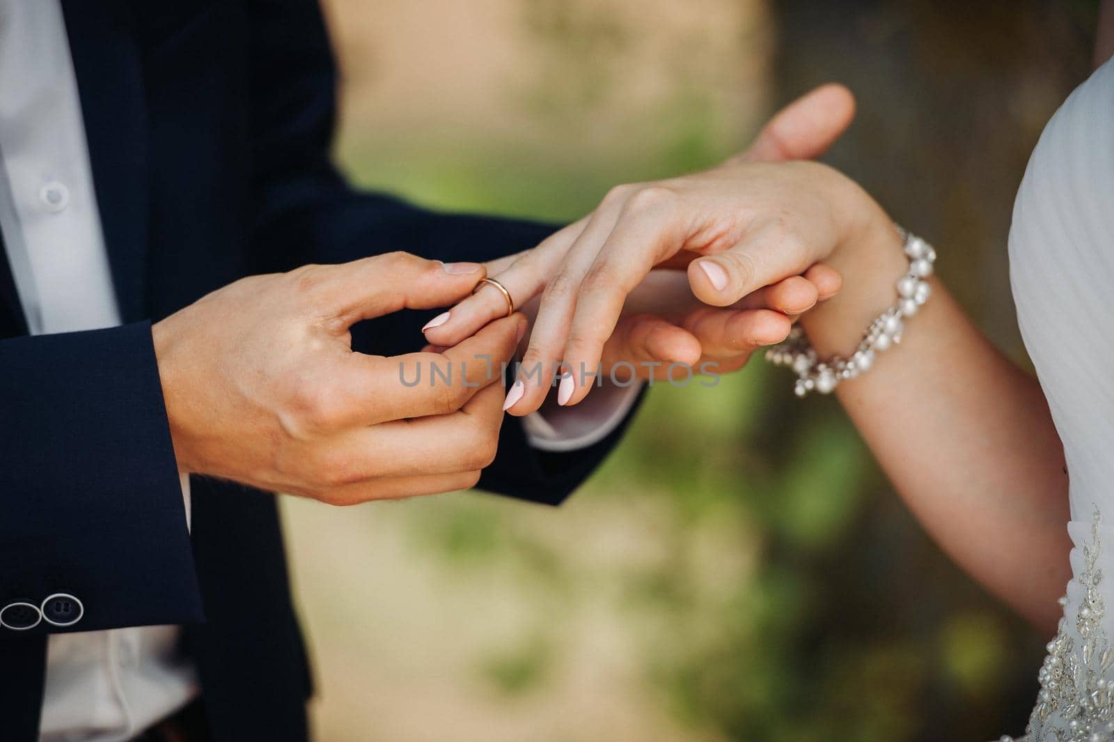 The groom puts an engagement ring on the bride's finger on their wedding day.