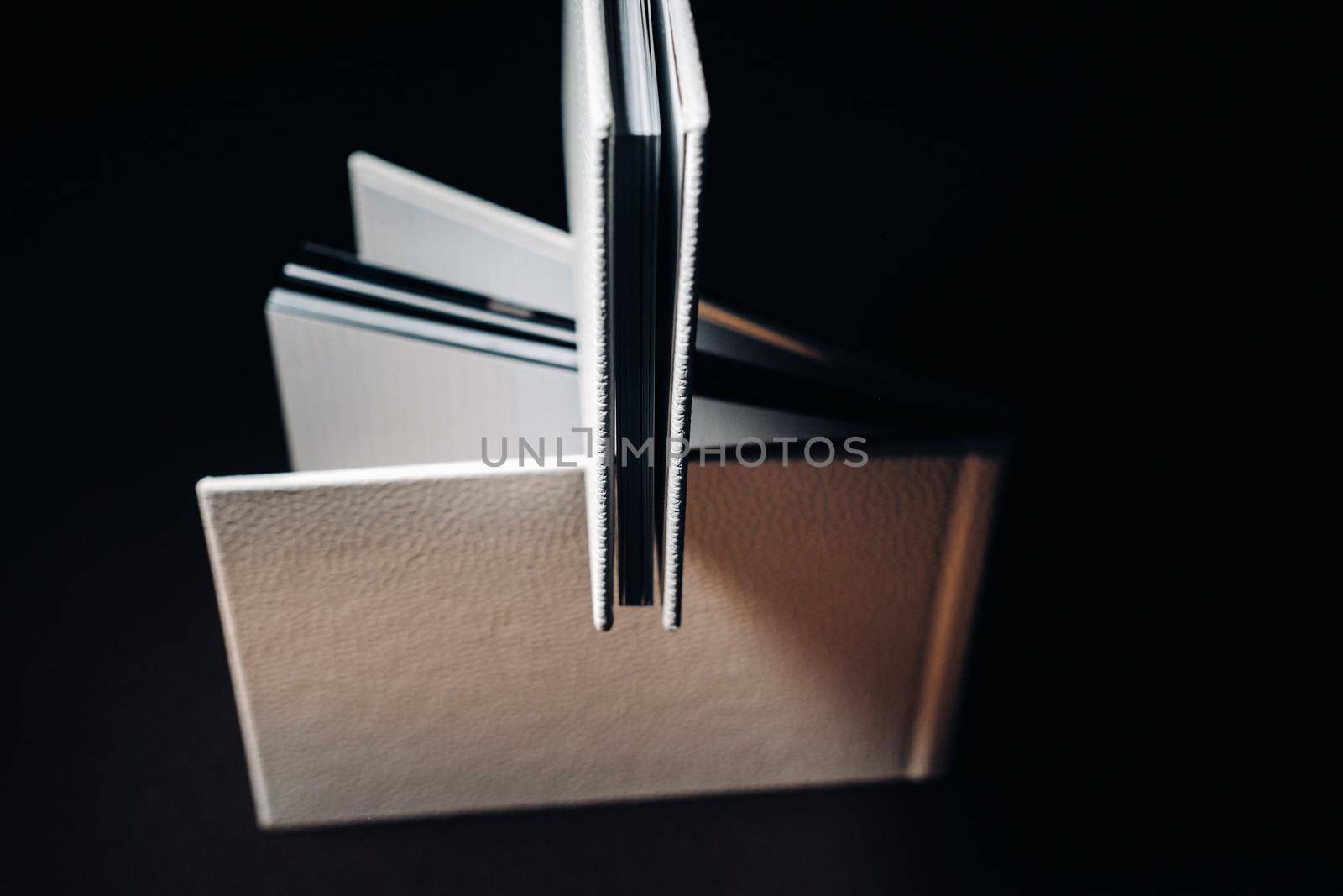 Composition of photo books in natural white leather of different sizes. The white paper on a dark background