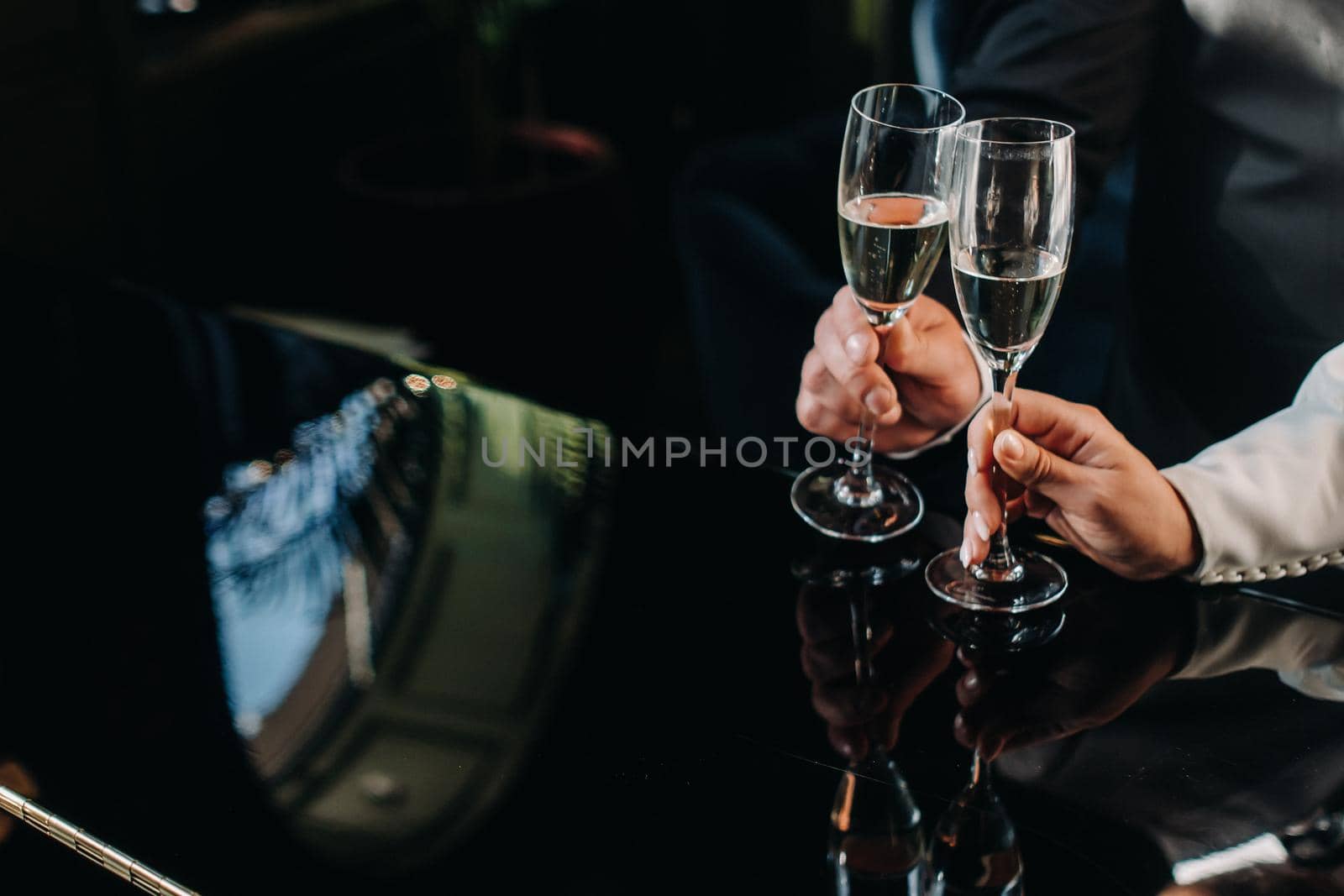 A man and a woman hold champagne glasses in their hands close-up by Lobachad