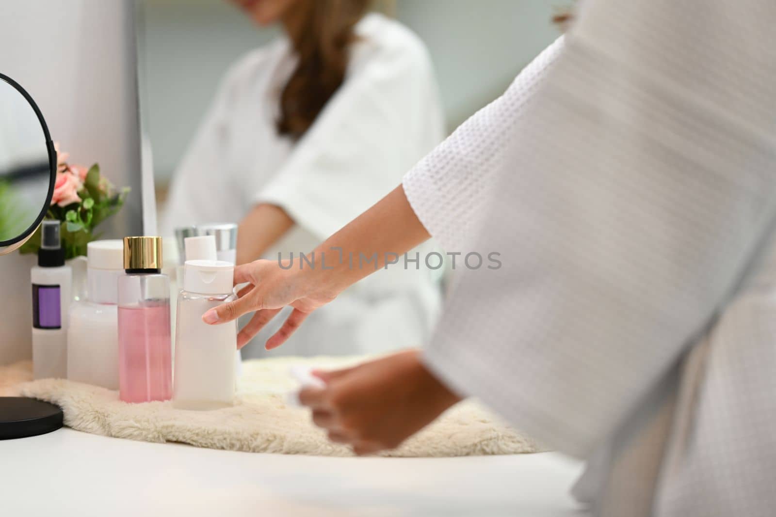 Cropped shot of woman in bathrobe choosing cosmetic package on dresser table. Beauty treatment and self care concept.