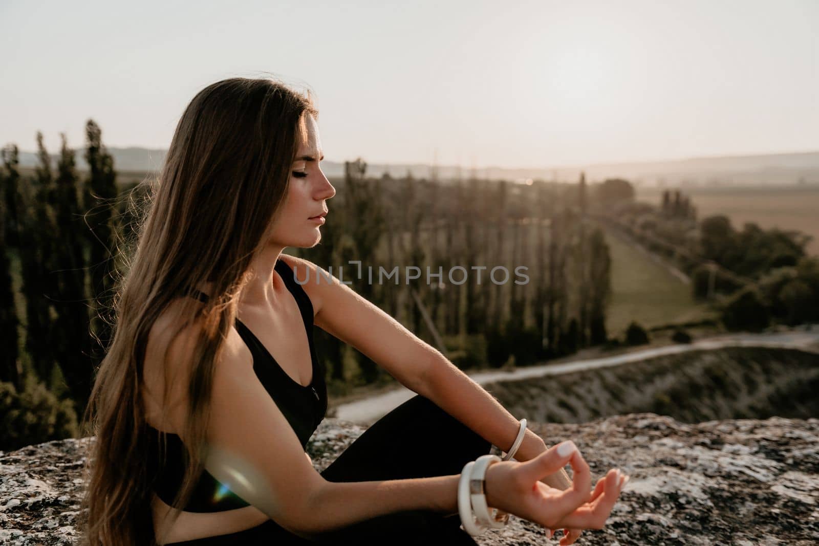 Well looking middle aged woman with long hair, fitness instructor in leggings and tops doing stretching and pilates on the rock near forest. Female fitness yoga routine concept. Healthy lifestyle.