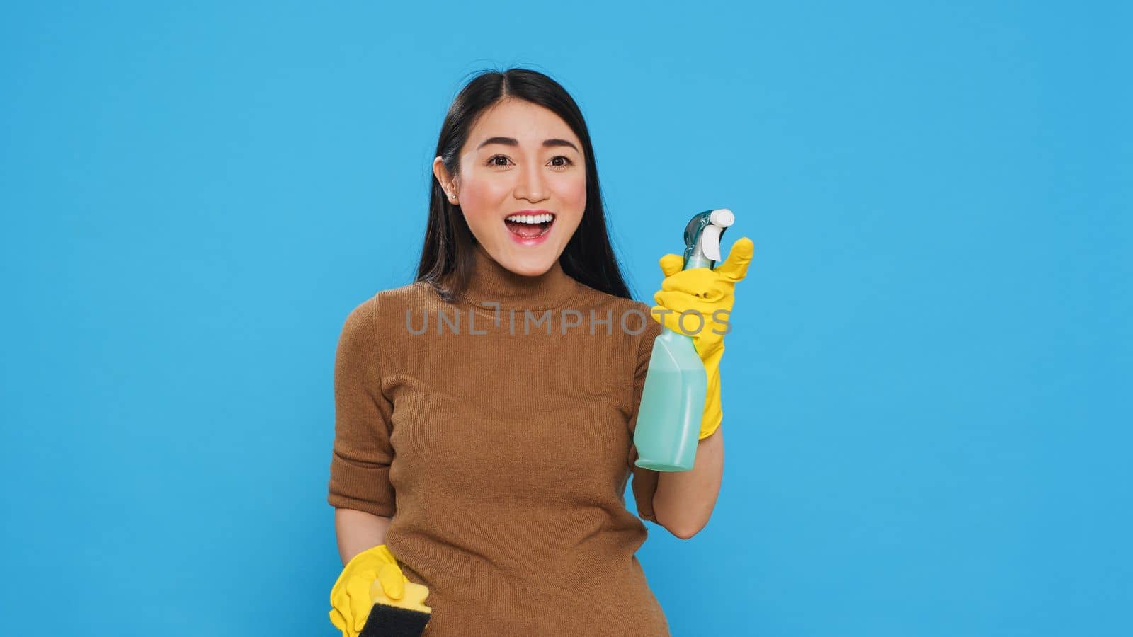 Professional housekeeper being amazed about how good is detergent spray while cleaning house for her clients. Asian maid committed to maintaining the highest standards of cleanliness and hygiene