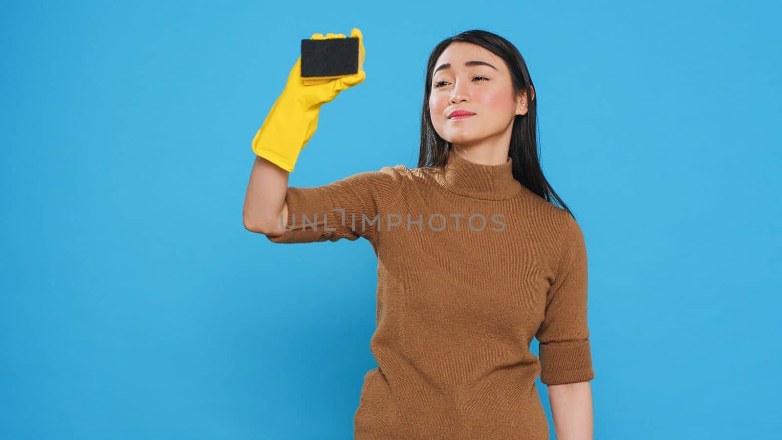 Smiling maid using sponge and professional cleaning detergent while cleaning customer house, using cleanliness equipment. Cleaner wore gloves as part of her attire while doing the housework.