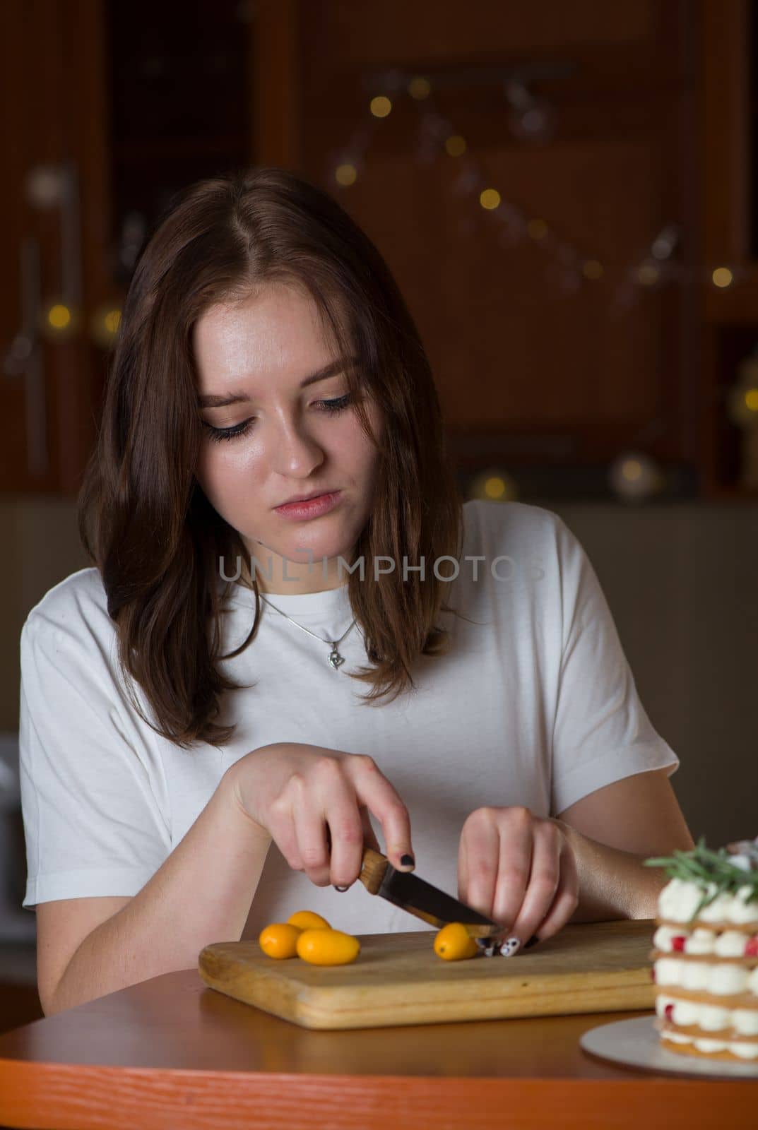 Girl cuts fresh kumquat citrus on a wooden board on the kitchen table. The concept of healthy food, culinary arts, vegetarianism, diet.