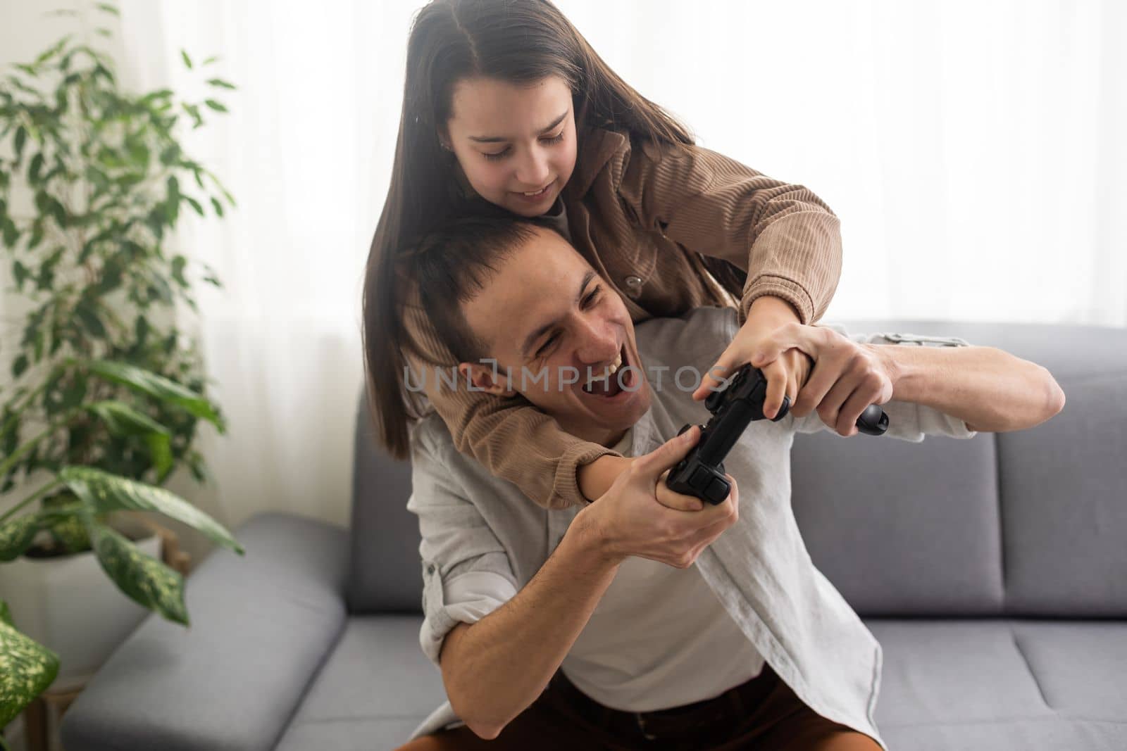 A father and a little daughter play video games using gamepads at home. A man and a child hold game joysticks in their hands. The family is having fun in the bedroom while being quarantined