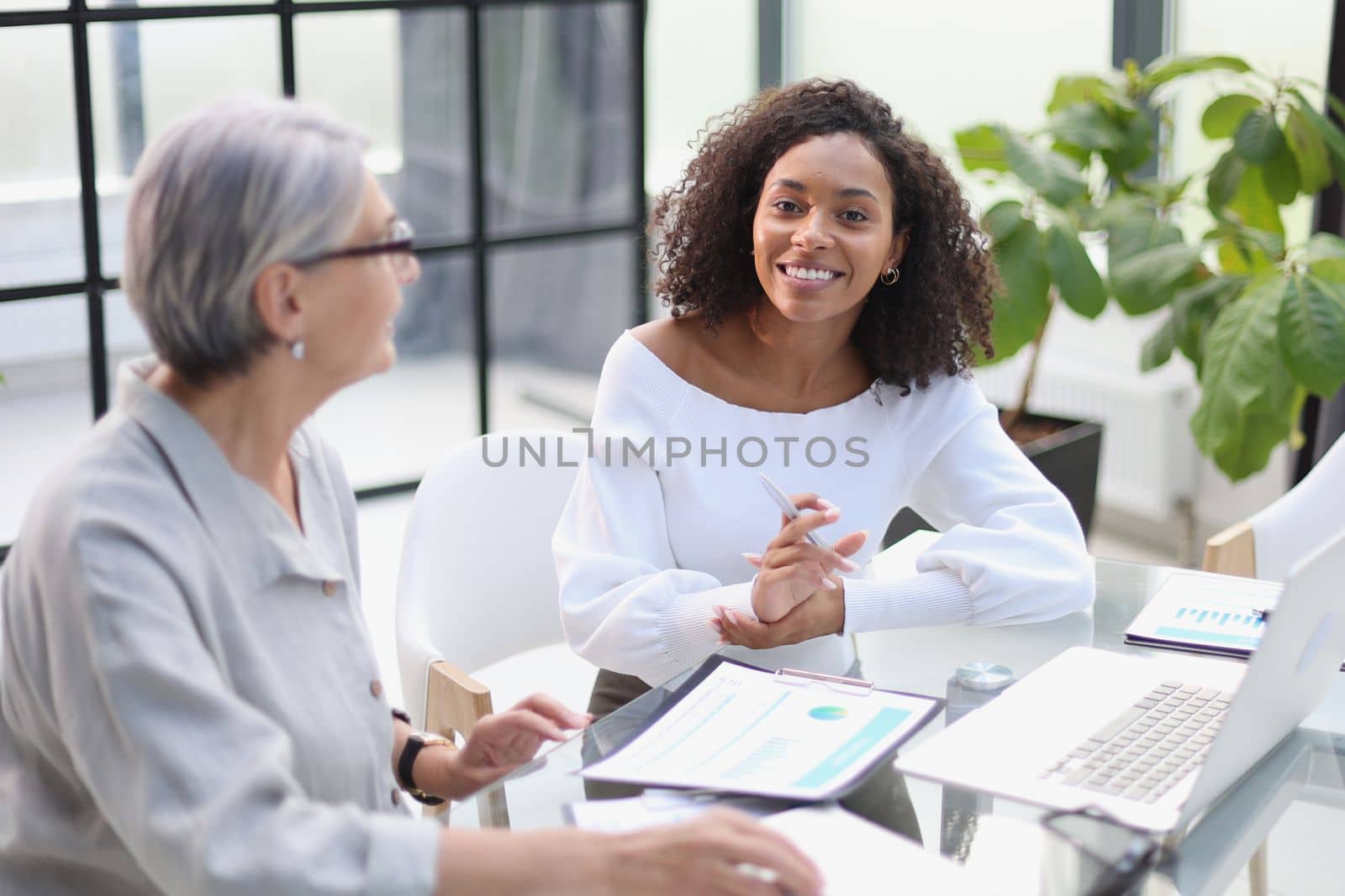 Business women smile while working together on a laptop at a table in the boardroom in the office