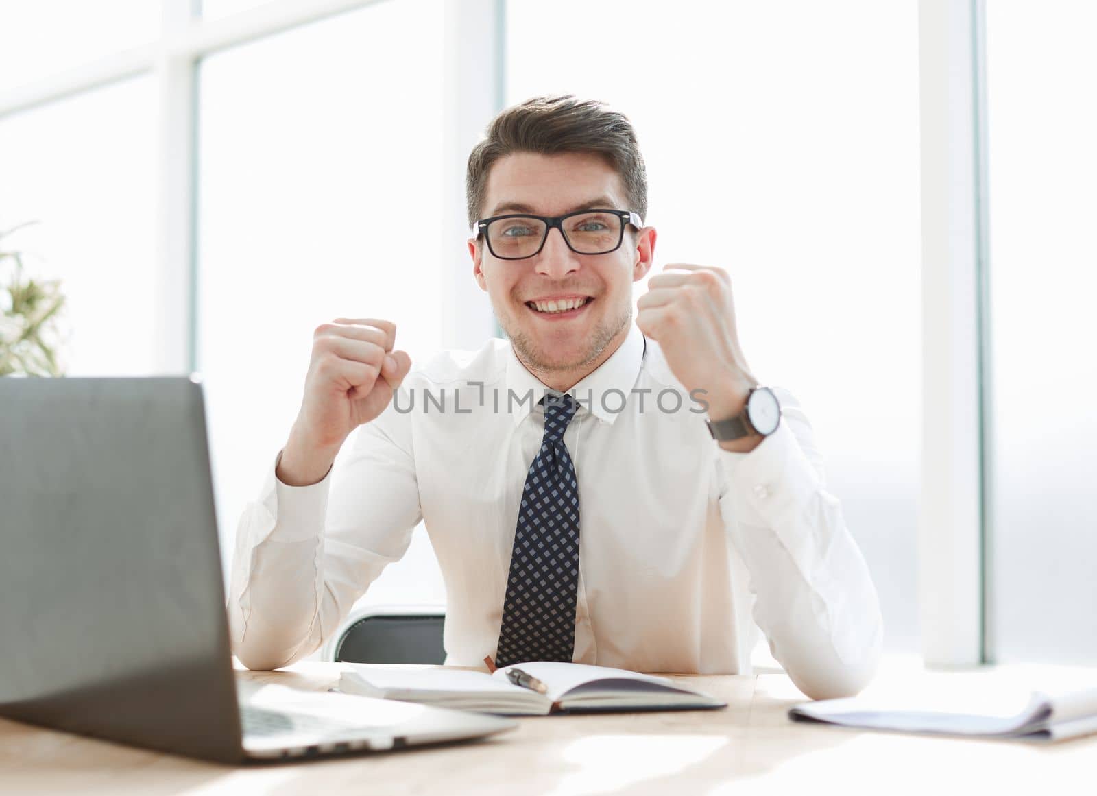 Happy young businessman raising hands in front of laptop