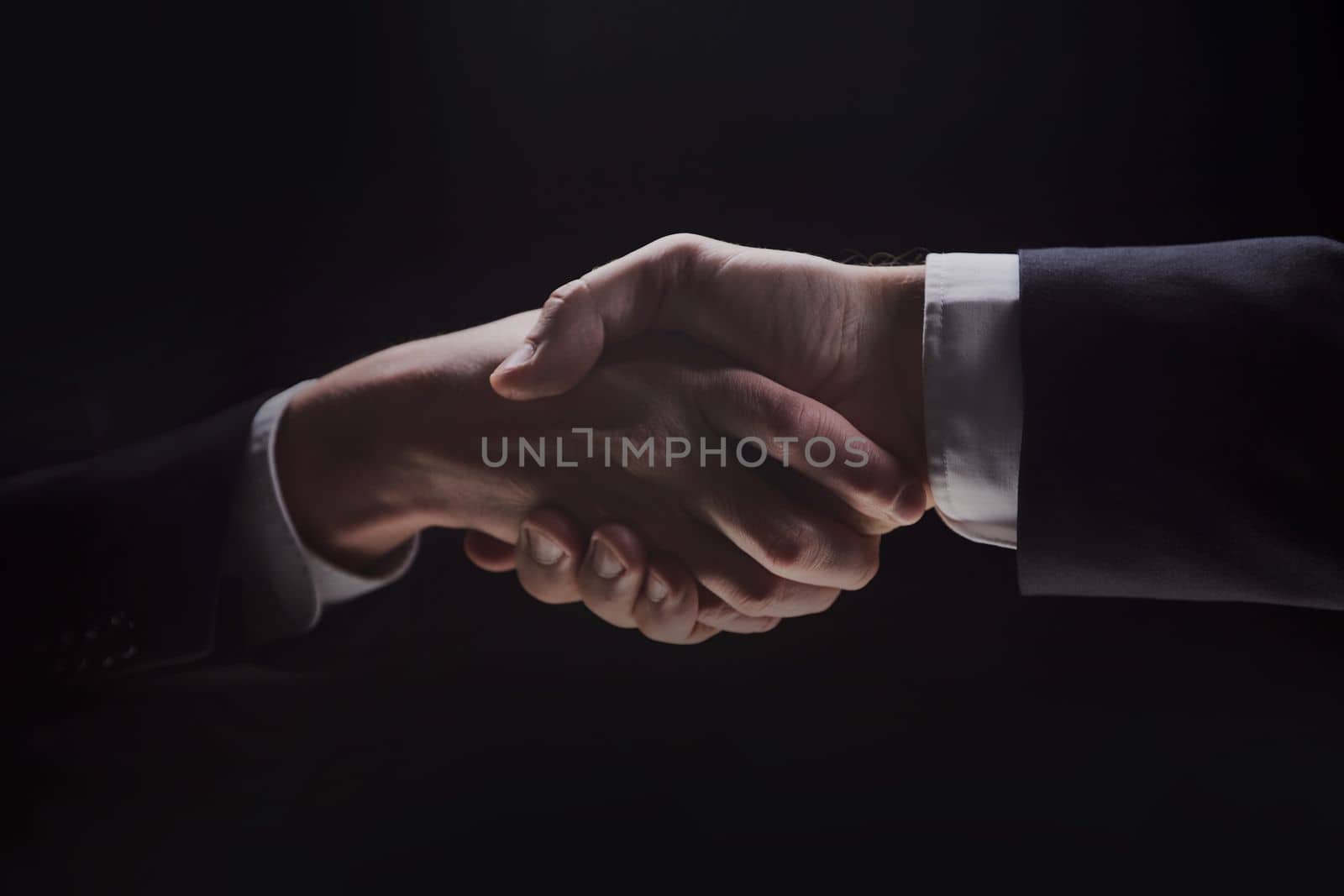 Photo of two men in suits shaking hands on a black background