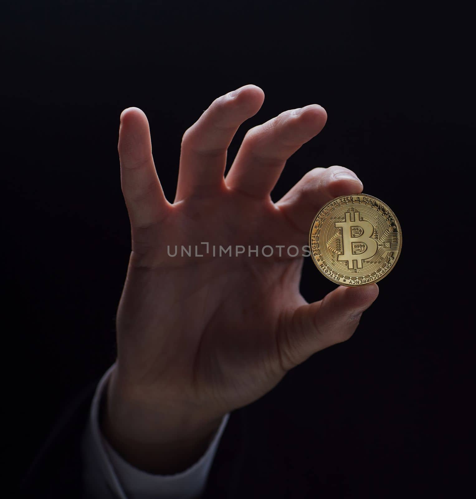 A hand holds a coin isolated on a black background.