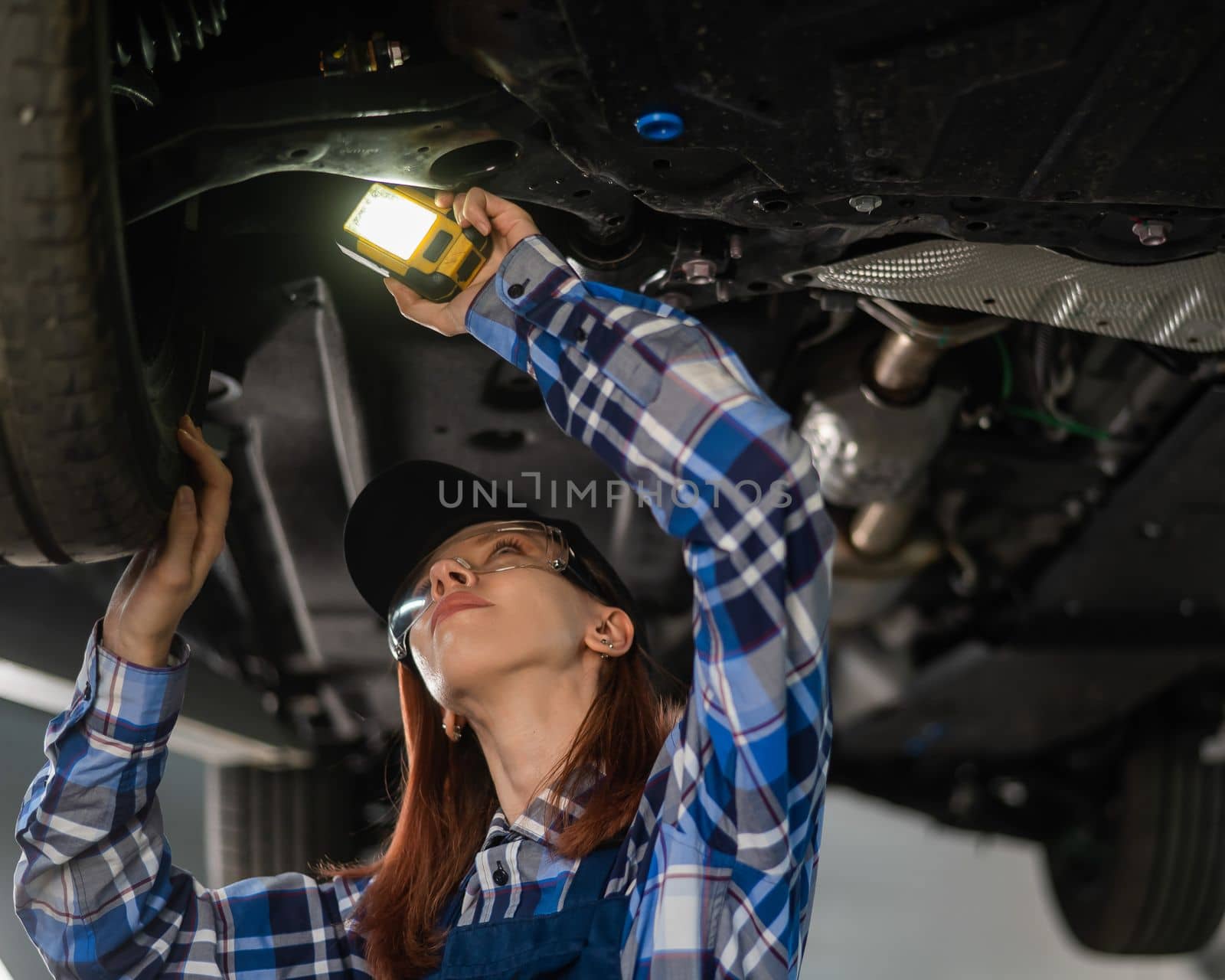 A female mechanic inspects a lifted car. A girl at a man's work