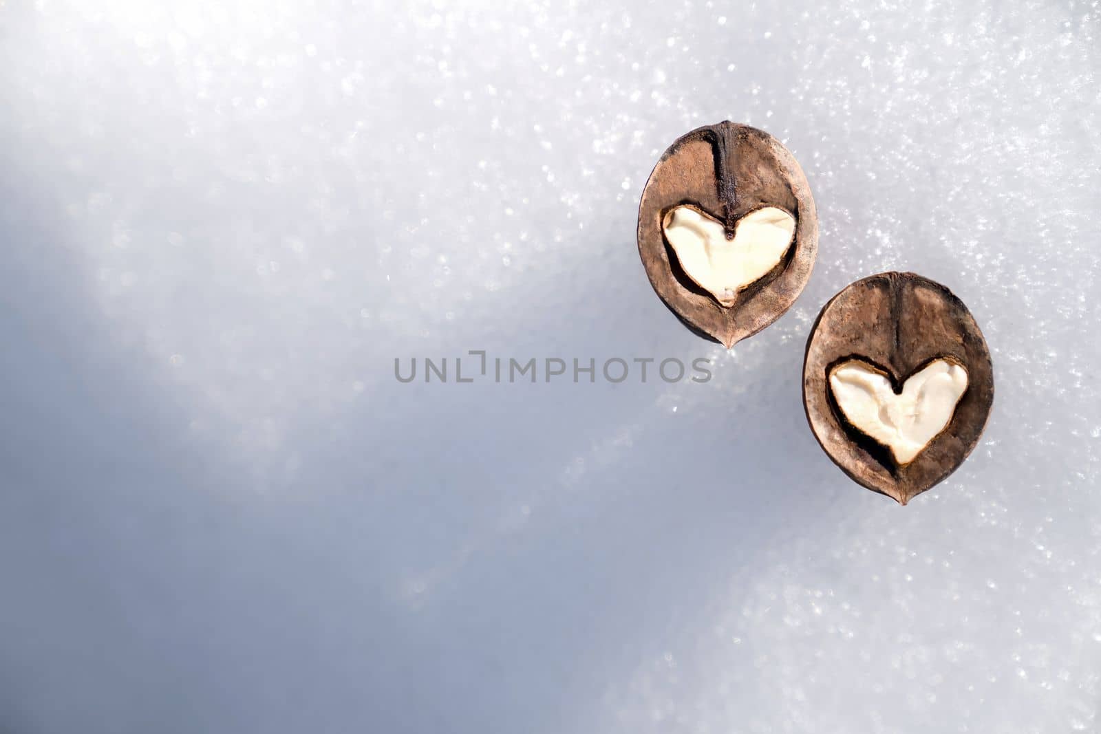 Two white hearts made of walnut halves against background of white snow, concept of Valentine's Day and health, copy space