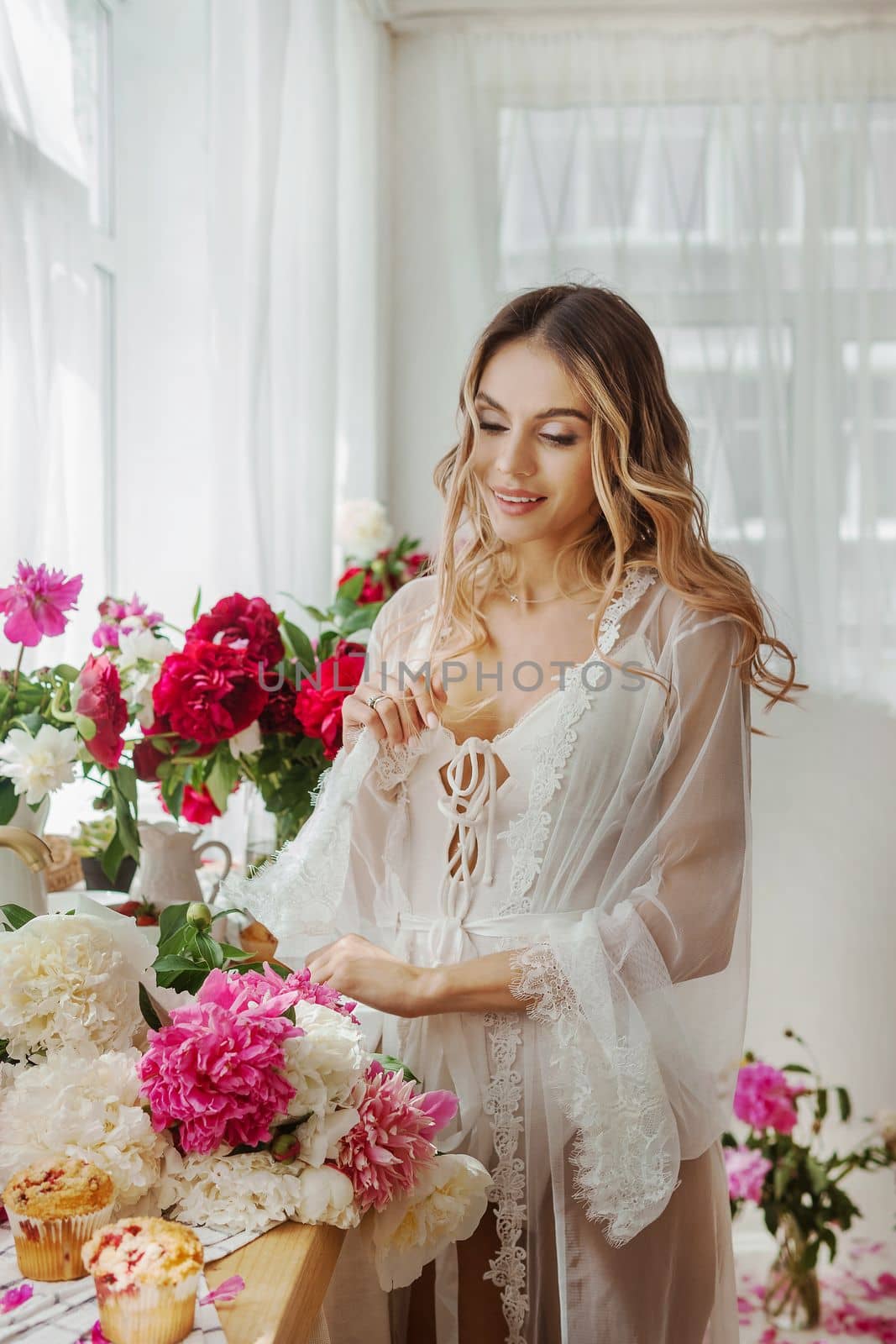 A beautiful girl in a white nightgown at home surrounded by spring flowers. A room decorated with bouquets of peonies. by Annu1tochka