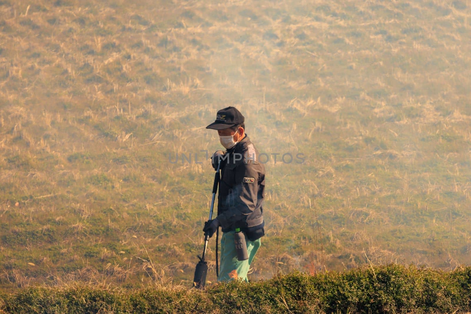 Hyogo, Japan - February 5, 2023: Fire fighter with flame thrower walks along fire line of controlled burn by Osaze