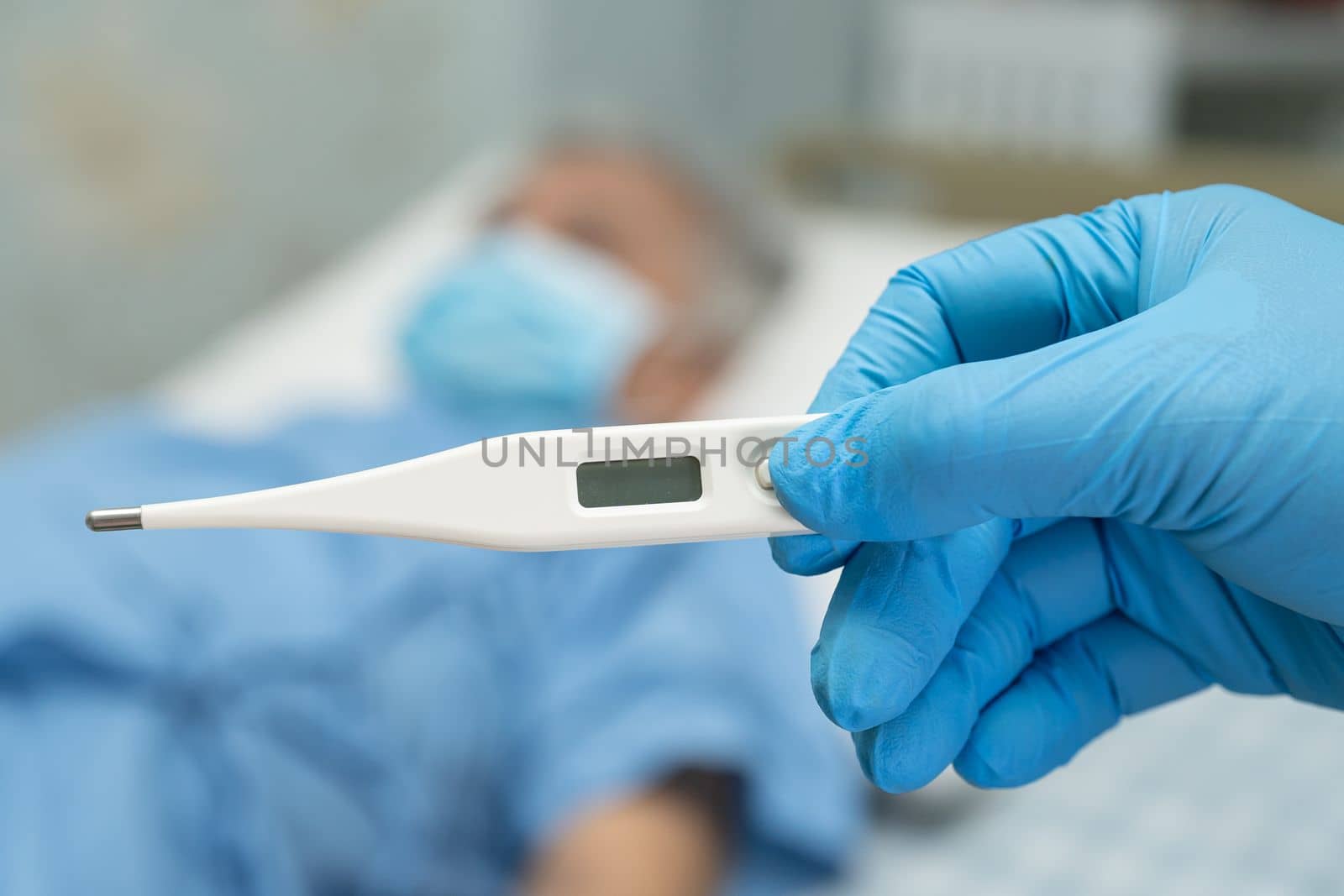 Doctor holding digital thermometer to measures asian elderly woman patient wearing a face mask have a fever in hospital, healthy strong medical concept. by pamai