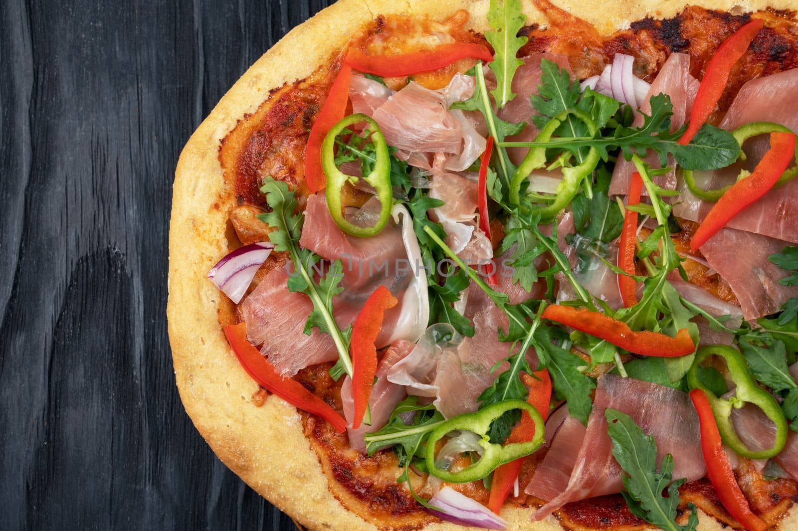 Italian Pizza on plate with jamon slices, pepper and fresh arugula leaves on top